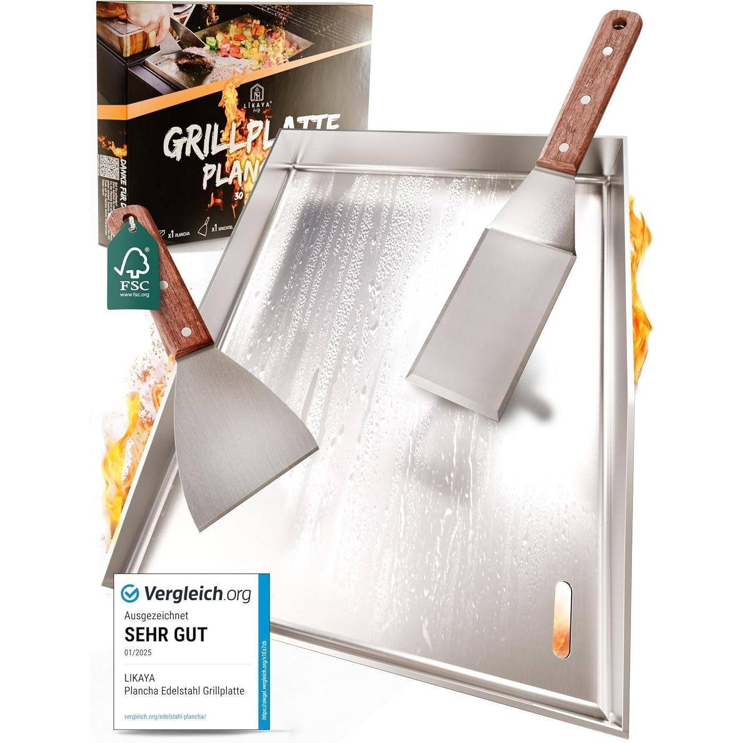 Grillplatte vom Typ 'Plancha' mit zwei Spateln auf einer Metalloberfläche. Im Hintergrund Verpackung und eine 'Sehr gut' Auszeichnungsetikette.