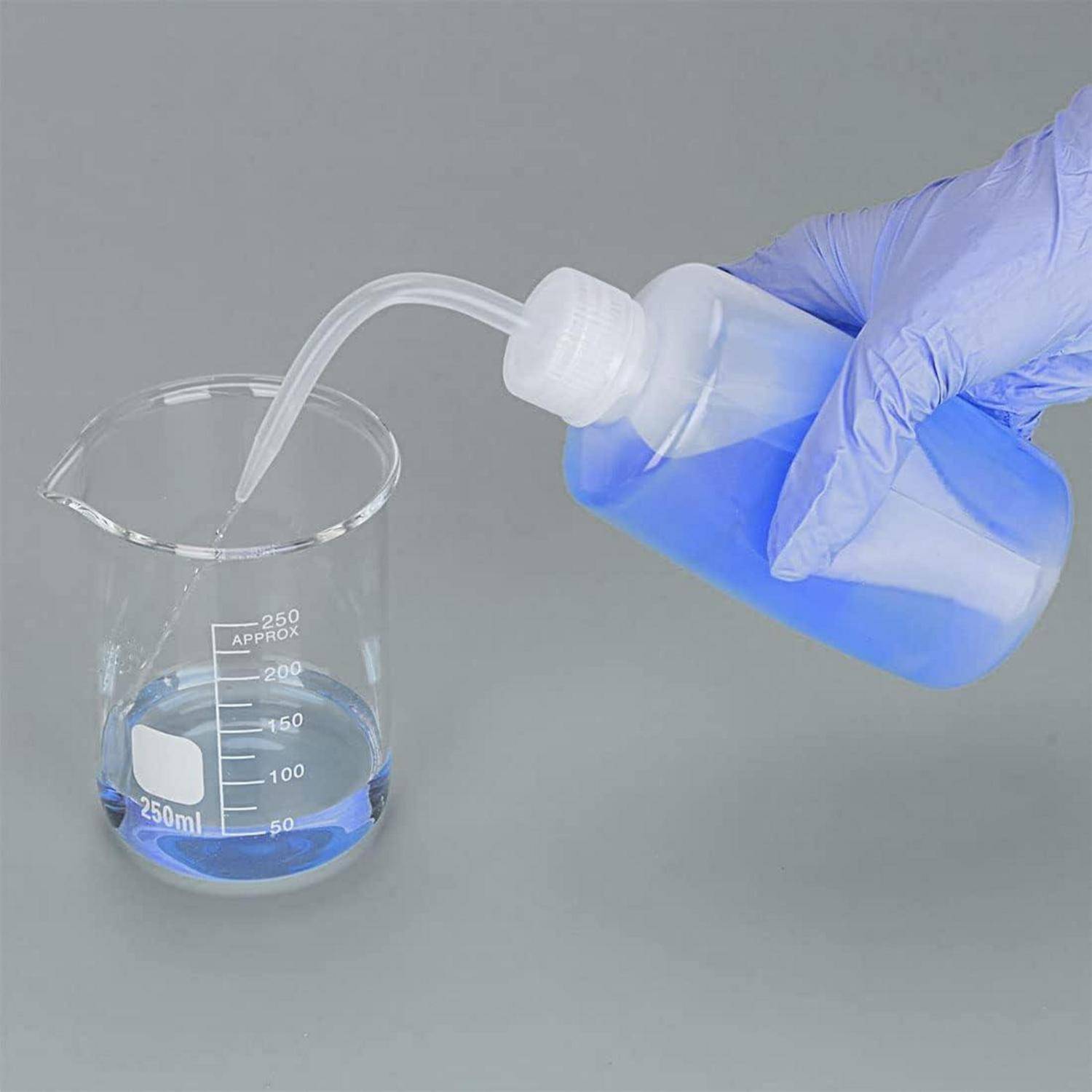 Eine Hand mit Handschuh gießt blaue Flüssigkeit aus einer Plastikflasche in einen 250-ml-Messbecher und demonstriert damit eine Laborumgebung oder ein Experiment.