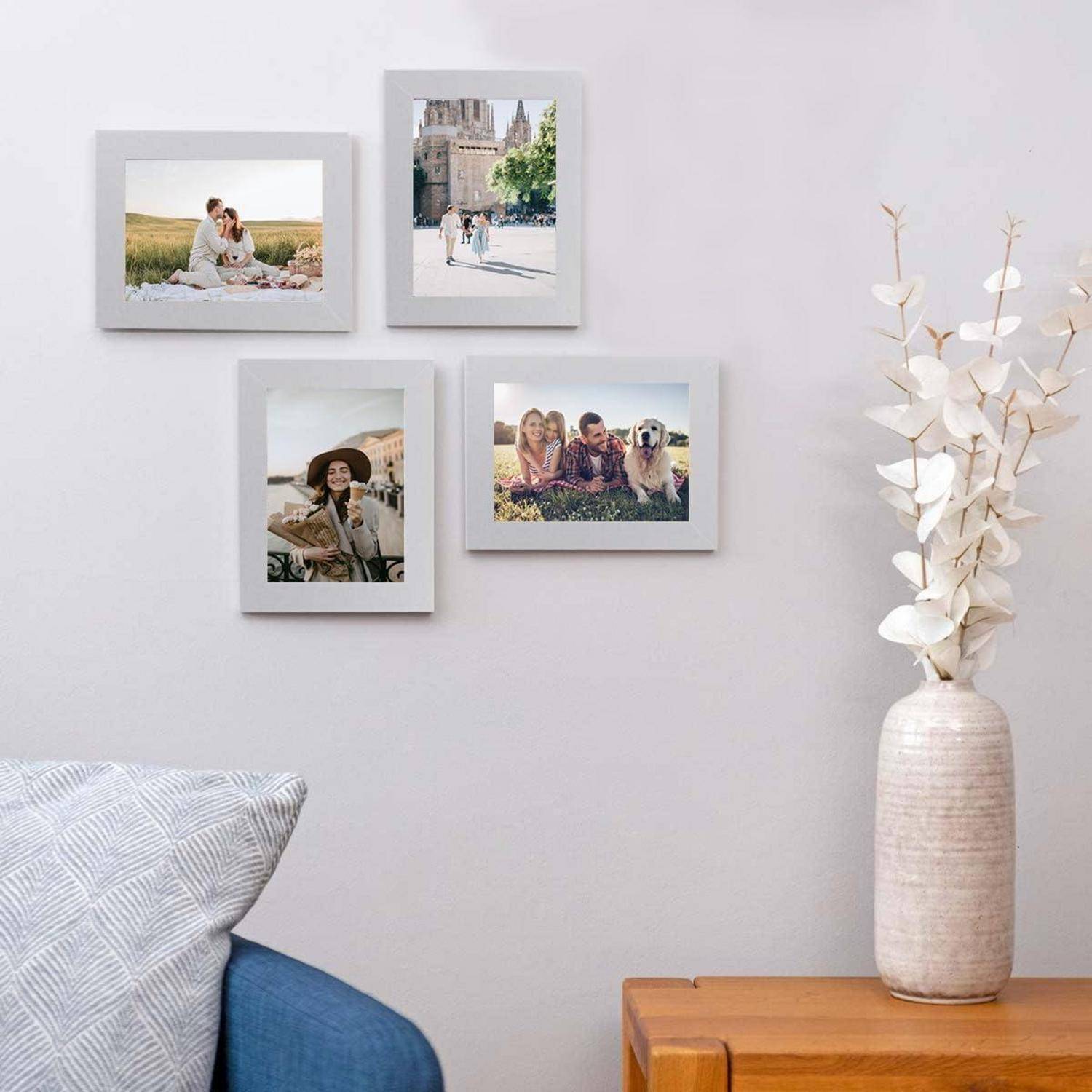 Vier gerahmte Familienfotos an einer grauen Wand, neben einer weißen Vase mit Zweigen. Ein blauer Kissenbezug ist teilweise auf einem Stuhl darunter sichtbar.