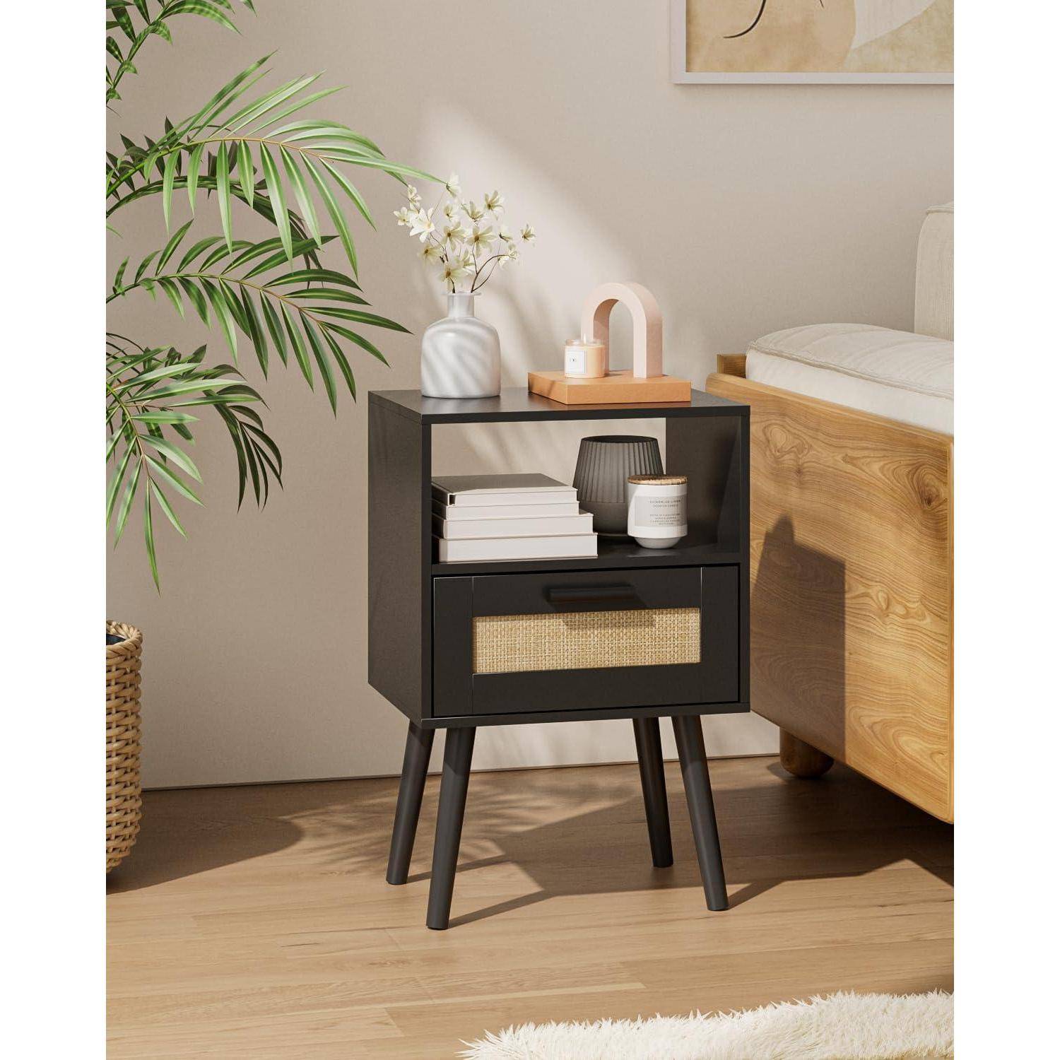 Ein kleiner, moderner schwarzer Nachttisch mit einer Schublade und einem offenen Regal, dekoriert mit einer Blumenvase, einer kleinen Lampe und Büchern, neben einem Sofa.