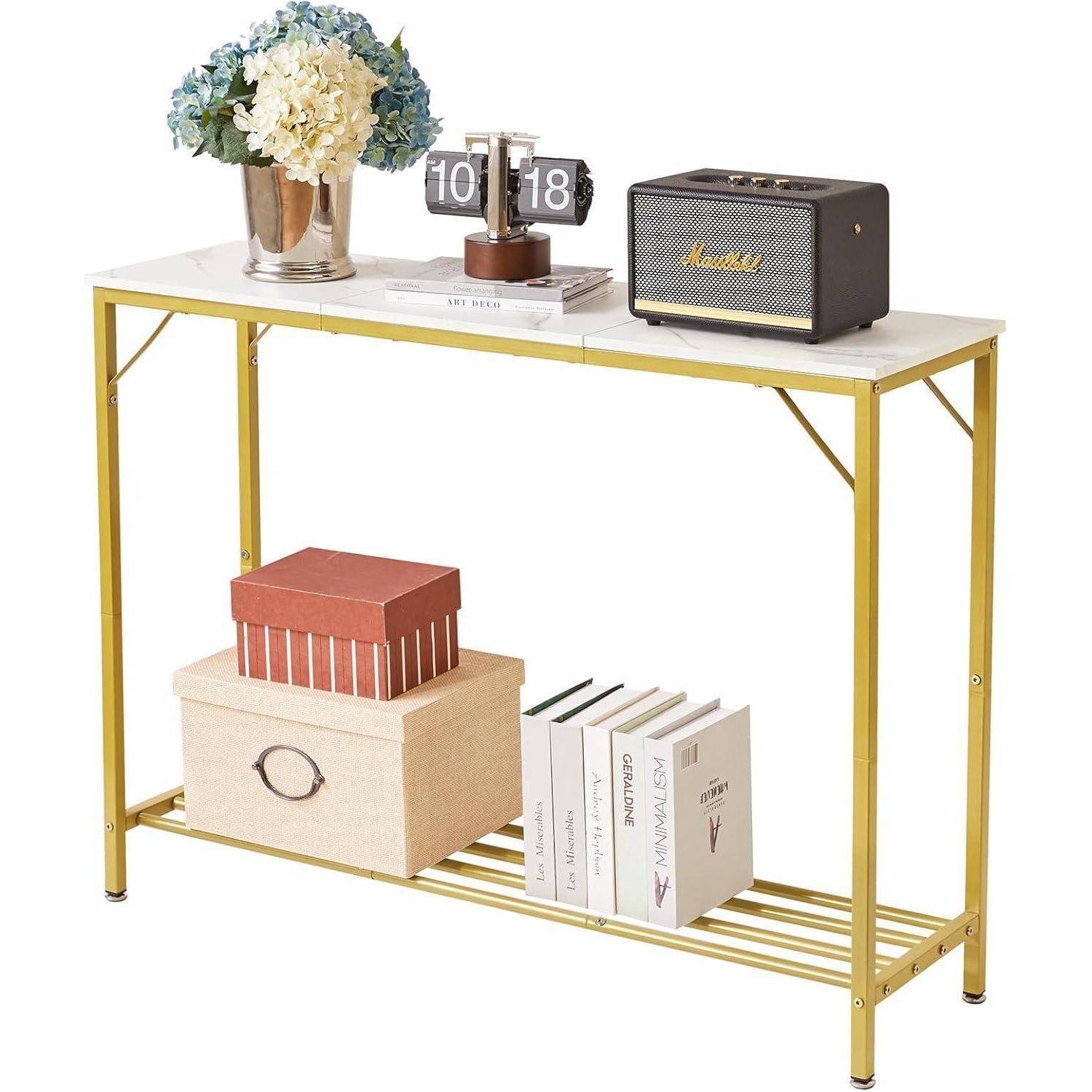 Ein moderner Konsolentisch mit goldenem Rahmen und weißer Platte trägt Bücher, Dekorboxen, einen im Vintage-Stil gehaltenen Kalender, der '10 18' anzeigt, eine Vase mit Blumen und einen kleinen Lautsprecher.