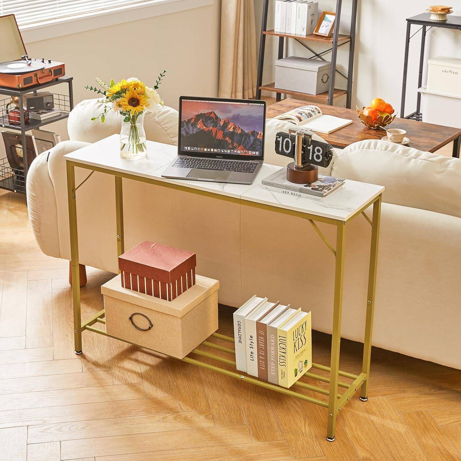 Wohnzimmer mit einem modernen Konsolentisch, auf dem ein geschlossener Laptop, Bücher und eine Box stehen. Sonnenblumen befinden sich auf dem Tisch, mit Sofas und Dekoration im Hintergrund.