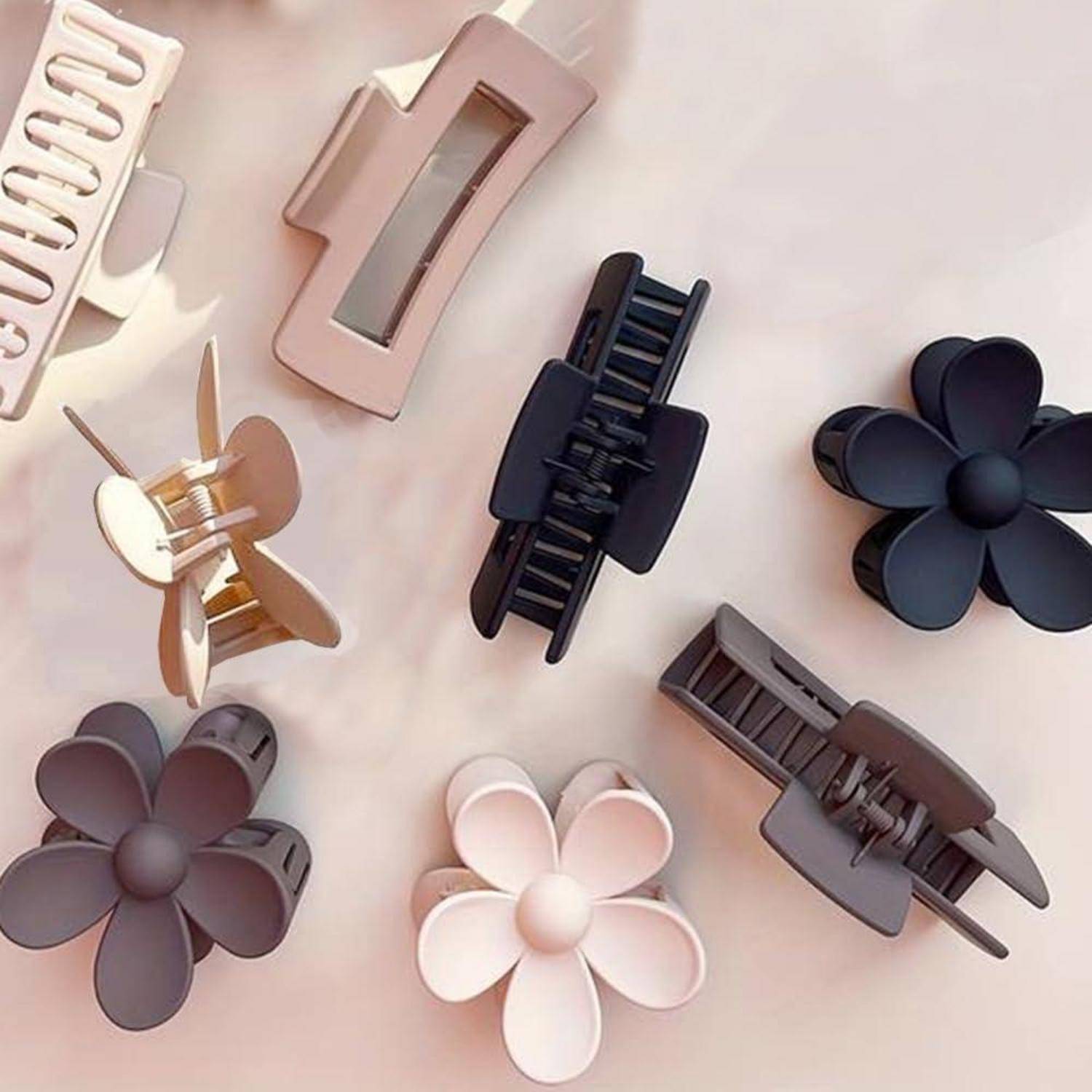 Eine Sammlung von Haarspangen in verschiedenen Formen und neutralen Farben, darunter floristische und geometrische Designs, auf einer hellen Oberfläche angeordnet.