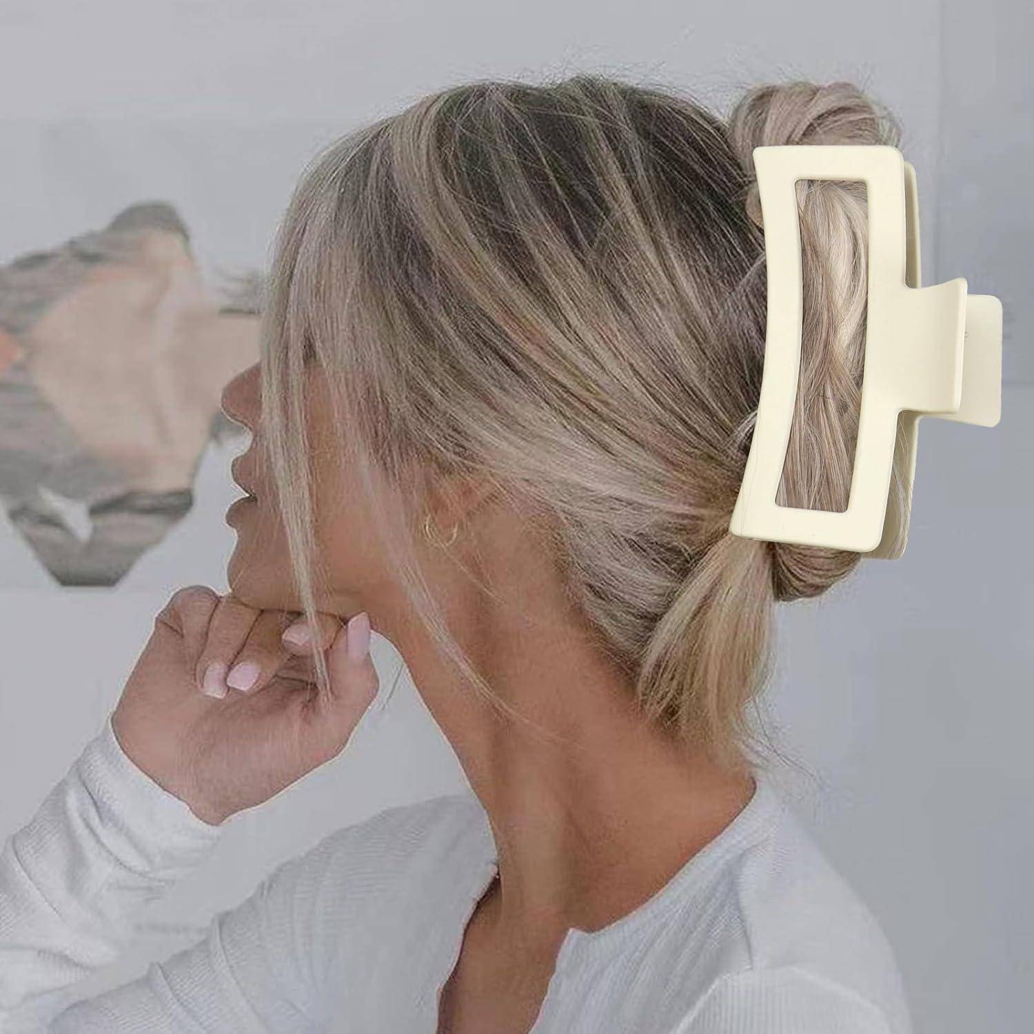 Eine Frau mit blonden, zu einem großen, beigen Haarclip hochgesteckten Haaren; halb abgewandt. Im Hintergrund verschwommene Wandkunst.