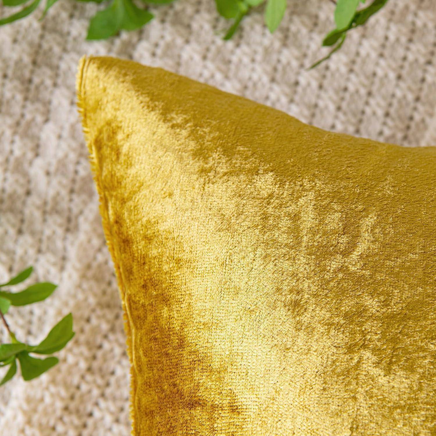 Ein goldener Samtkissen auf einer beigen texturierten Oberfläche, umgeben von grünen Blättern.