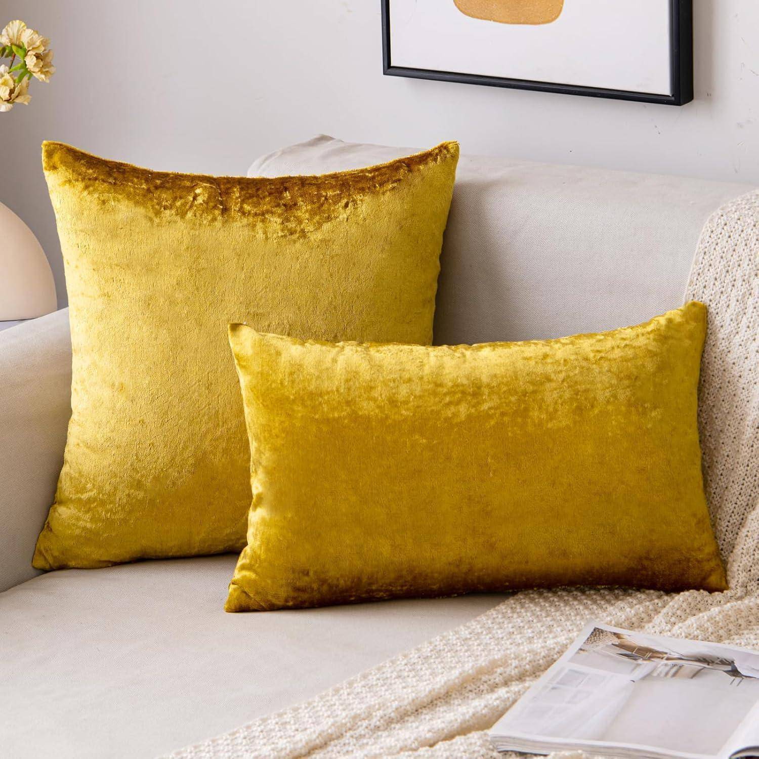 Zwei gelbe Samtkissen auf einem hellgrauen Sofa, mit einer beigen gestrickten Decke in der Nähe, die eine gemütliche und einladende Atmosphäre schafft.