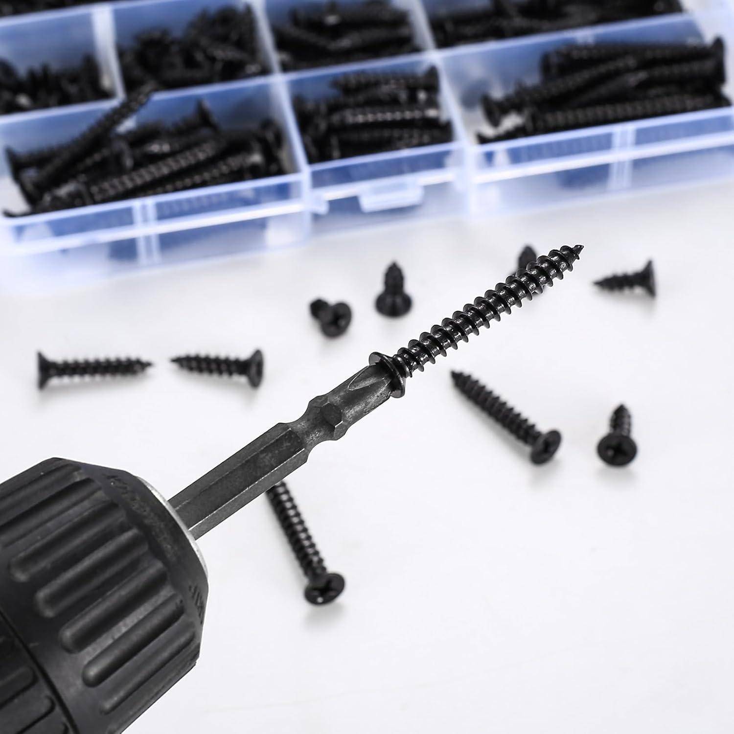 Eine schwarze Bohrerspitze hält eine Schraube im Fokus, während zahlreiche schwarze Schrauben auf einer weißen Oberfläche verstreut sind und Plastikfächer im Hintergrund mit Schrauben gefüllt sind.
