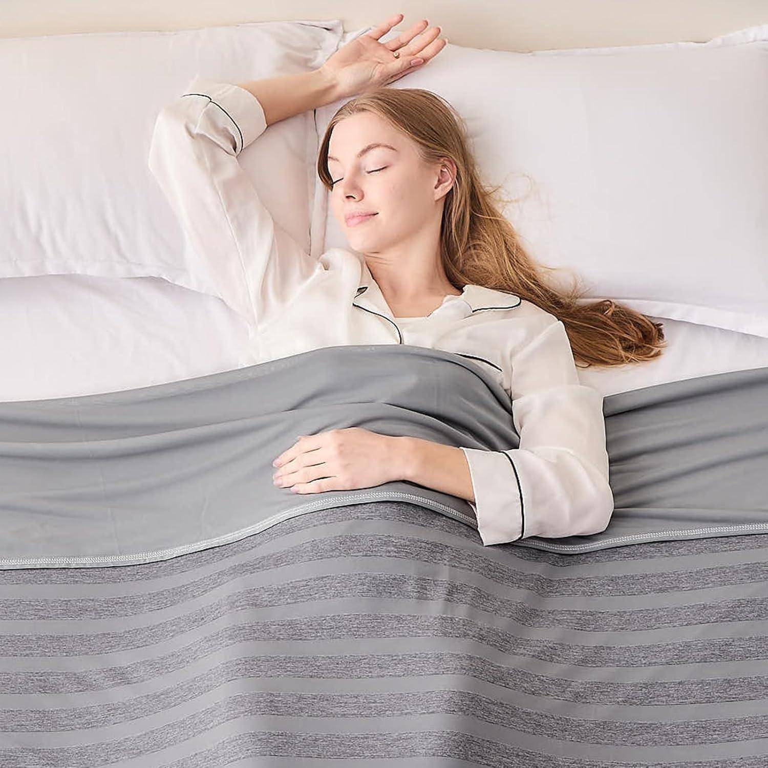 Eine Frau schläft friedlich in einem Bett, zugedeckt mit einer grauen Decke. Sie legt ihren Kopf auf ein weißes Kissen, mit einem Arm unter ihrem Kopf.