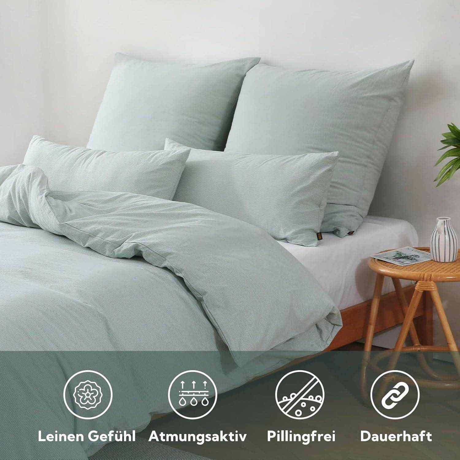 Ein ordentlich gemachtes Bett mit hellgrüner Bettwäsche, zwei großen Kissen und einem kleinen Beistelltisch mit einer Pflanze.Icons unterhalb zeigen Gewebeeigenschaften: Leinenoptik, atmungsaktiv, knitterfrei, strapazierfähig.