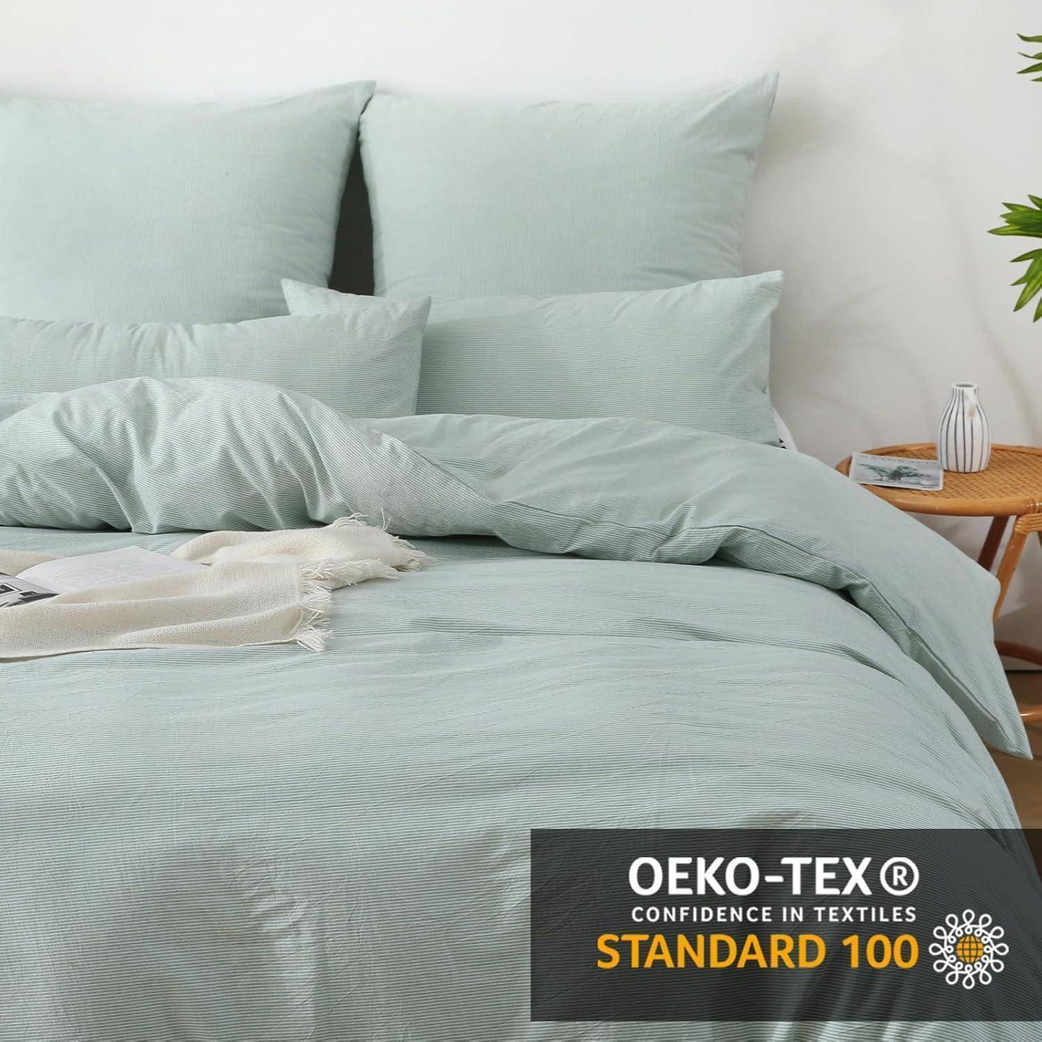Ein ordentlich gemachtes Bett mit hellgrüner Bettwäsche und Kissen. Auf dem Nachttisch stehen eine Pflanze und ein Buch. Ein 'Oeko-Tex Standard 100' Etikett ist sichtbar.