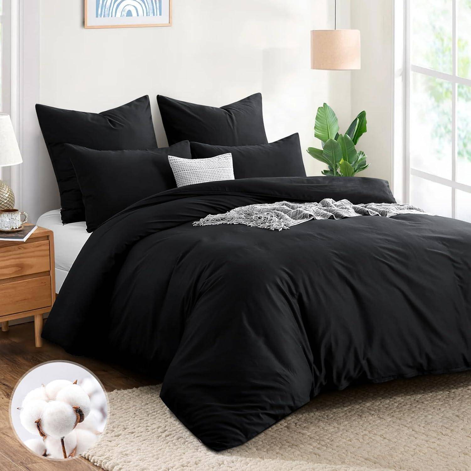 Ein Schlafzimmer mit einem ordentlich gemachten Bett, das mit einem schwarzen Bettüberwurf und Kissen bezogen ist, ein hölzerner Nachttisch mit einer Lampe und eine Pflanze in der Nähe des Fensters.