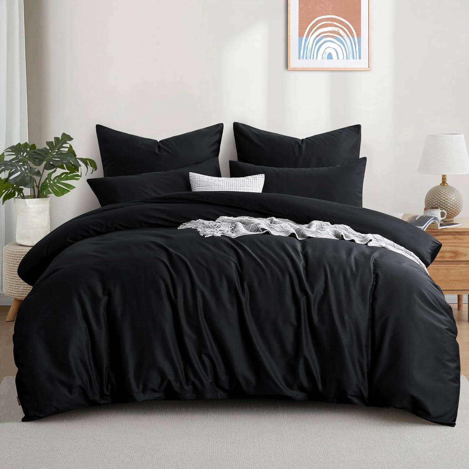 Ein ordentlich gemachtes Bett mit schwarzer Bettwäsche, drei Kissen und einem kleinen karierten Kissen. In der Nähe eine Pflanze, eine Lampe und ein gerahmtes abstraktes Kunstwerk an der Wand.