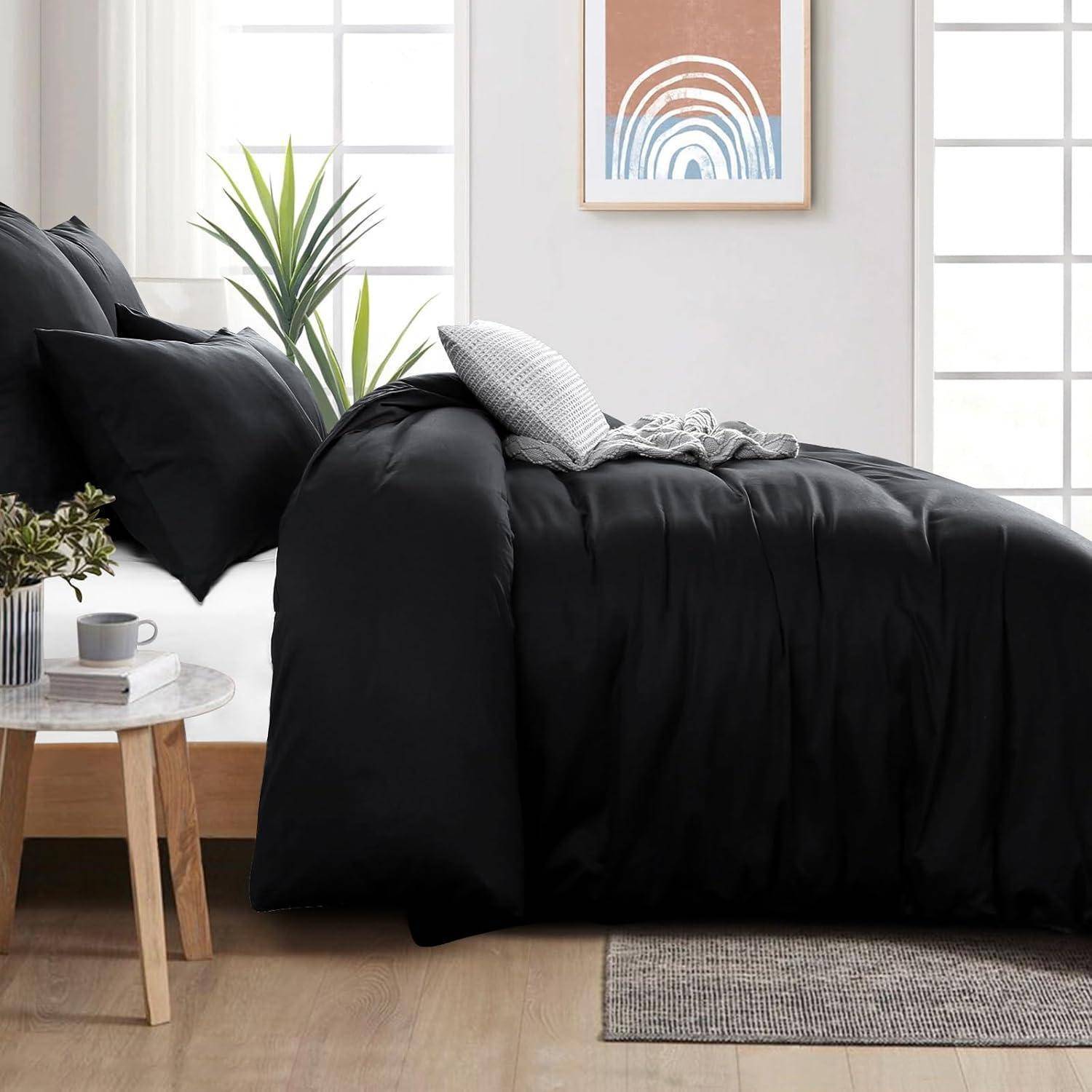 Ein modernes Schlafzimmer zeigt eine dunklefarbene Bettdecke auf einem Bett mit Kissen, einen kleinen Nachttisch mit einer Pflanze und einer Tasse sowie gerahmte Kunstwerke an der Wand.