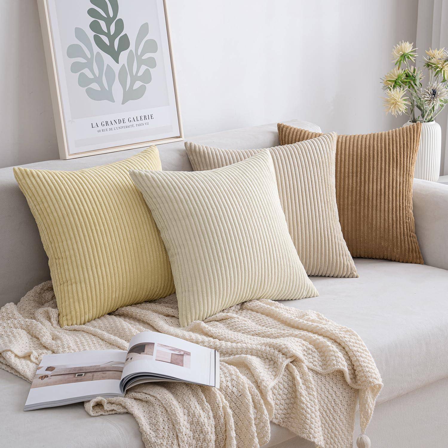 Eine gemütliche Wohnzimmerszene mit einem beigen Sofa, strukturierten Kissen in neutralen Tönen, einer warmen Decke und einem gerahmten botanischen Druck.