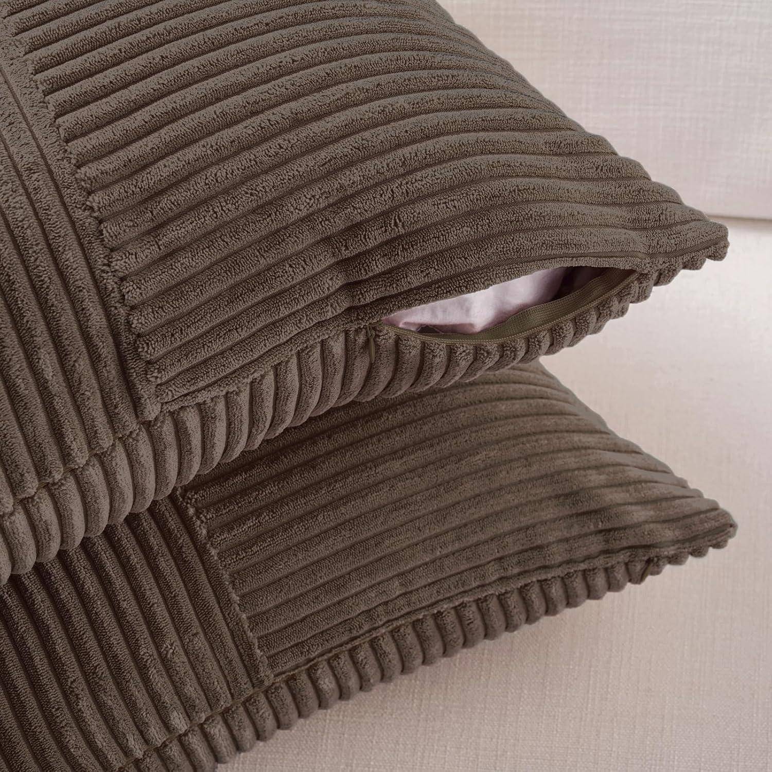 Zwei braune Cordkissen, die auf einem beigen Sofa gestapelt sind.