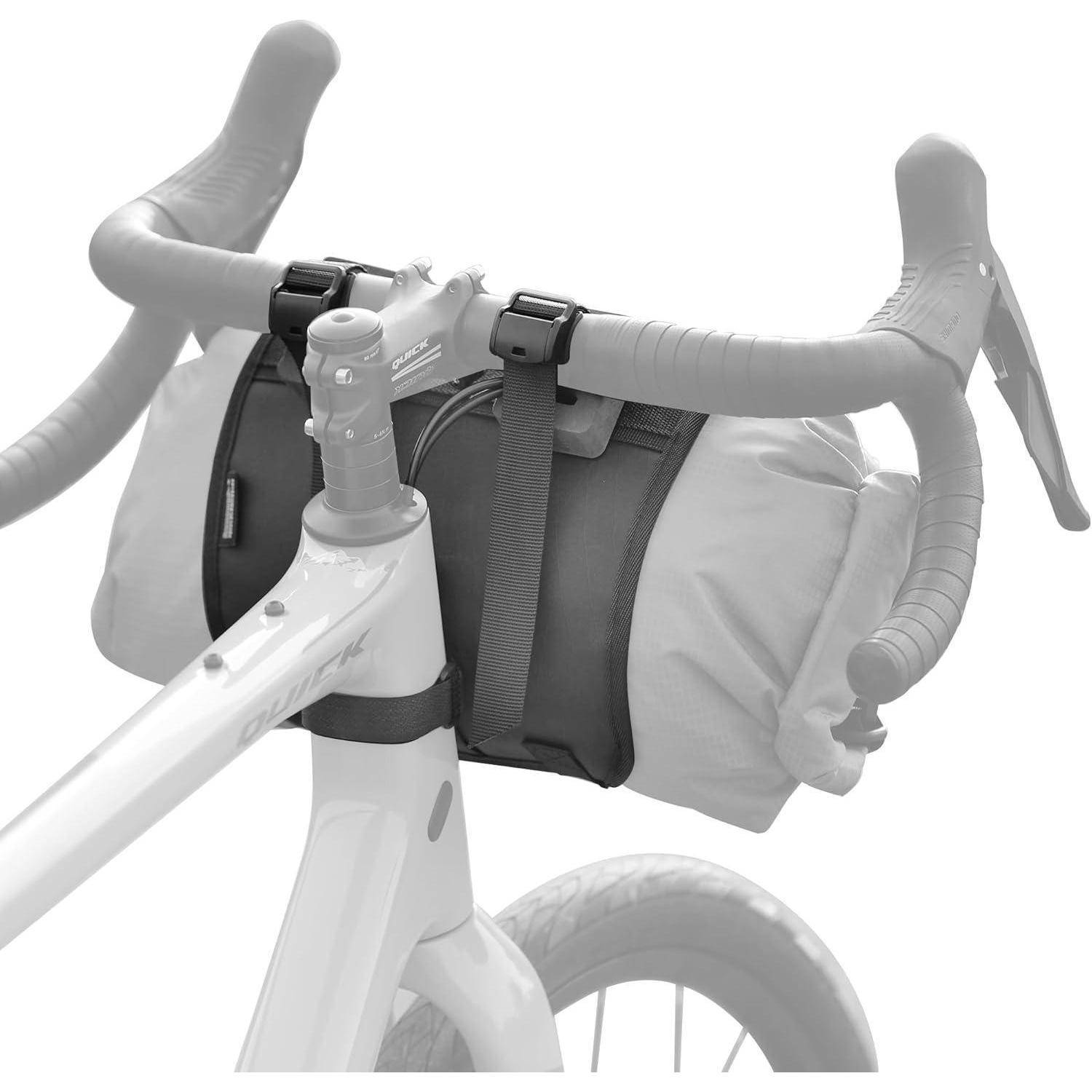Die Fahrradlenker halten eine gesicherte zylindrische Tasche. Der weiße Rahmen und die umgreifenden Lenkerbügel deuten auf eine Ausrüstung für Radtouren oder den Pendelverkehr hin.