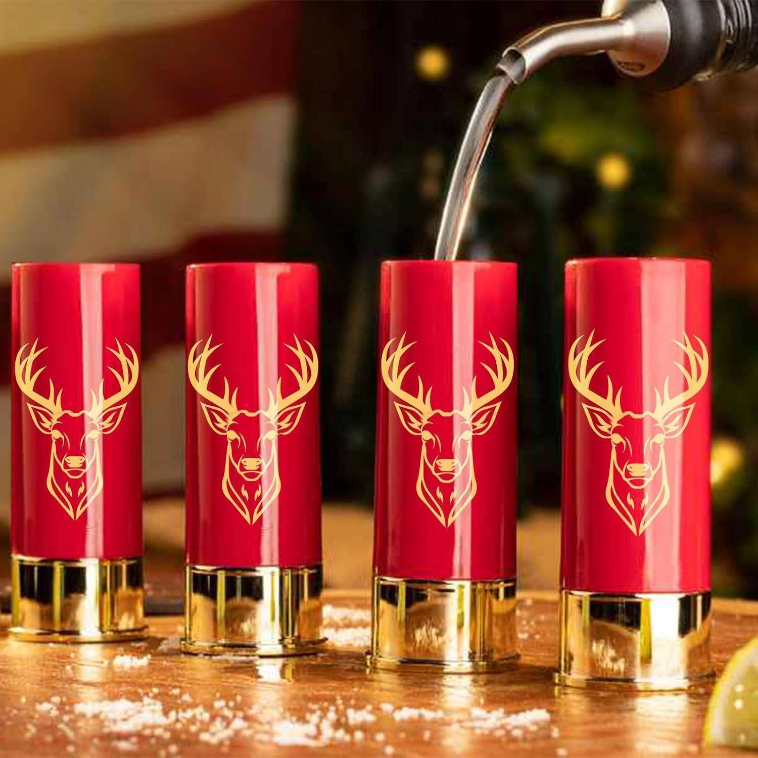 Eine Nahaufnahme von vier roten Schrotpatronenschnapsgläsern mit einem goldenen Hirschkopfdesign. In ein Glas wird Flüssigkeit eingegossen. Warme, festliche Atmosphäre.