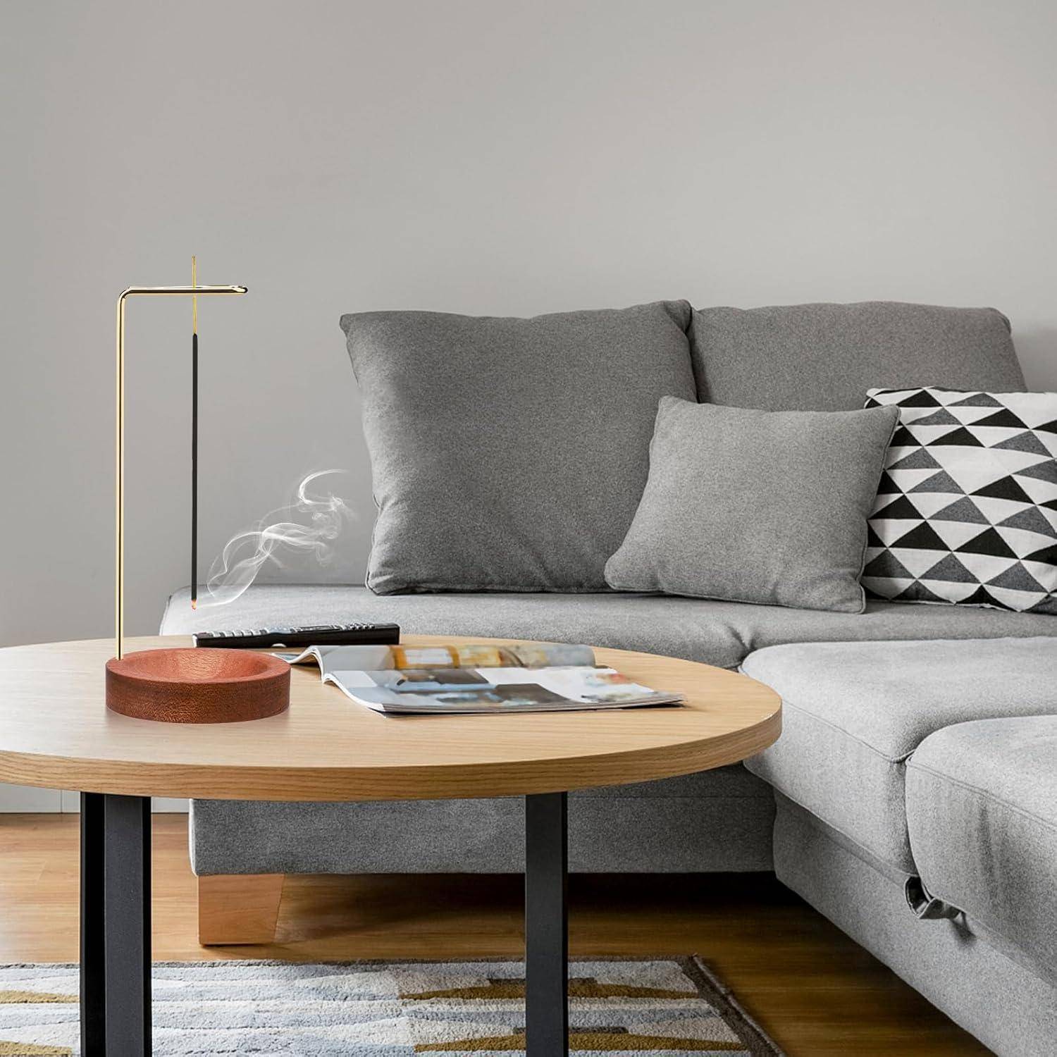 Ein gemütliches Wohnzimmer mit einem grauen Sofa, gemusterten Kissen, einem Holzcouchtisch und einer eleganten Lampe. Ein Buch und ein Tablett liegen auf dem Tisch.
