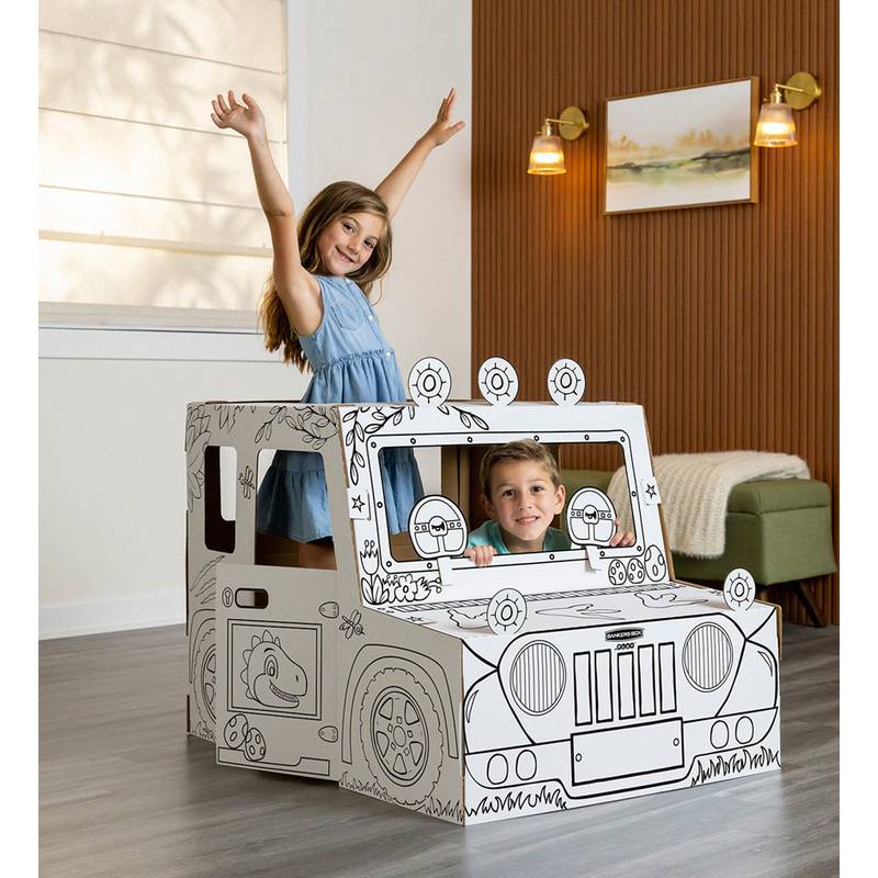 Ein junges Mädchen hebt ihre Arme neben einem lächelnden Jungen in einem Spielzeugauto aus Pappe in einem Wohnzimmer mit weißen Wänden und braunen Akzenten.