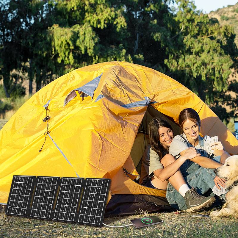 Zwei Personen sitzen vor einem gelben Zelt im Freien, mit einem tragbaren Solarpanel, das ein Gerät lädt, was auf einen umweltfreundlichen Campingausflug hindeutet.