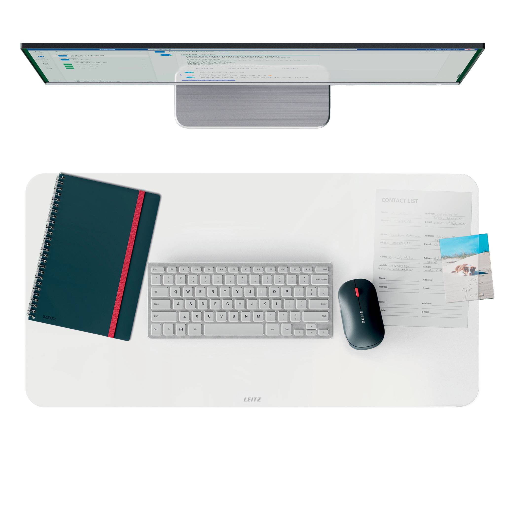 Overhead-Ansicht eines Desktop-Arbeitsplatzes mit Monitor, Tastatur, Maus, Notizbuch und Papieren auf einer weißen Schreibunterlage.