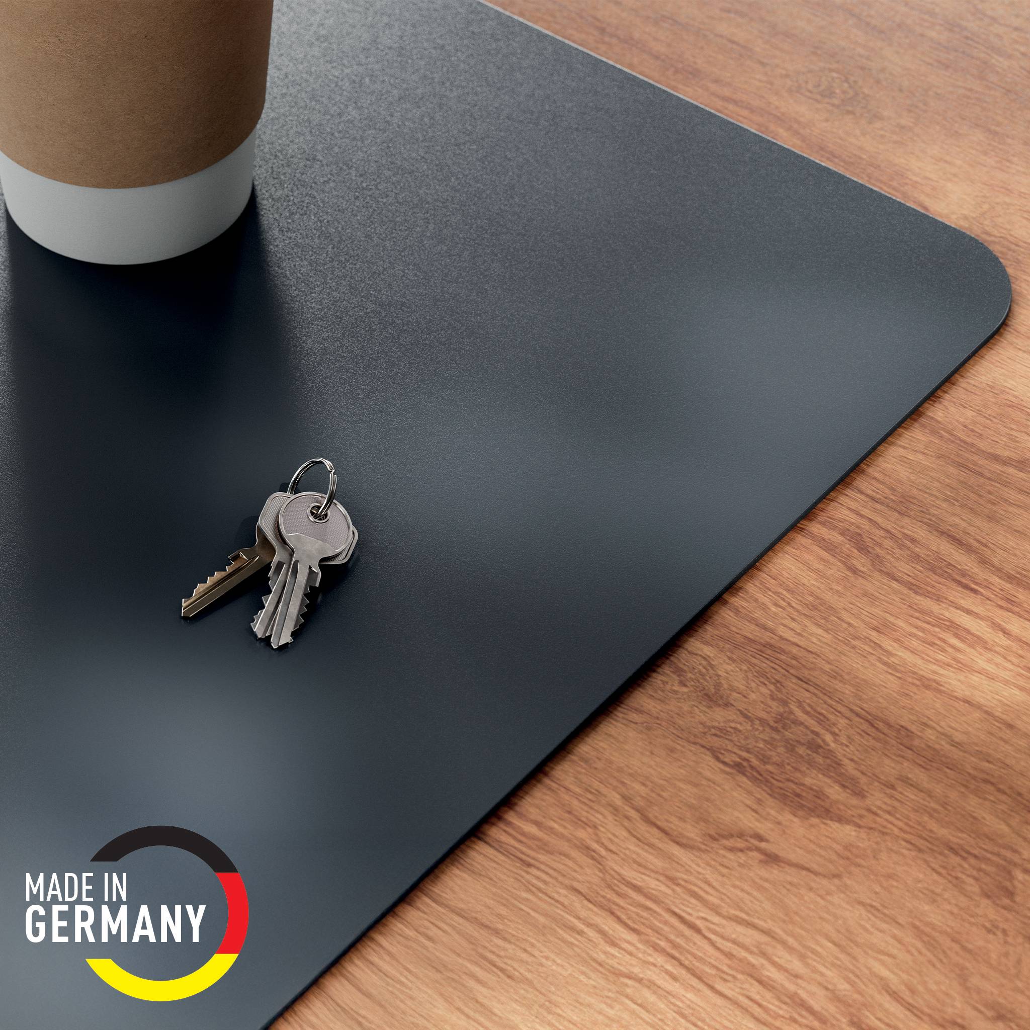 Schlüssel und eine Kaffeetasse auf einer schwarzen Schreibunterlage auf einer Holzoberfläche, mit einem 