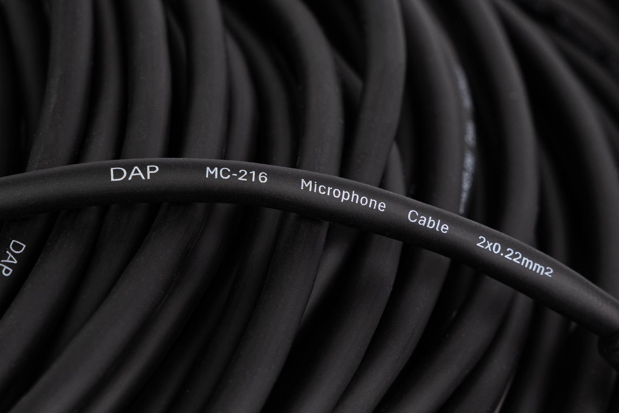Nahaufnahme eines aufgerollten schwarzen Mikrofonkabels mit der Beschriftung 'DAP MC-216 Mikrofonkabel 2x0.22'.