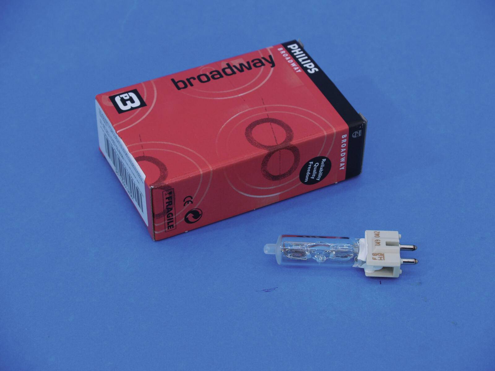 Eine Box und eine Halogenglühbirne auf einer blauen Oberfläche. Die Box ist mit „broadway PHILIPS