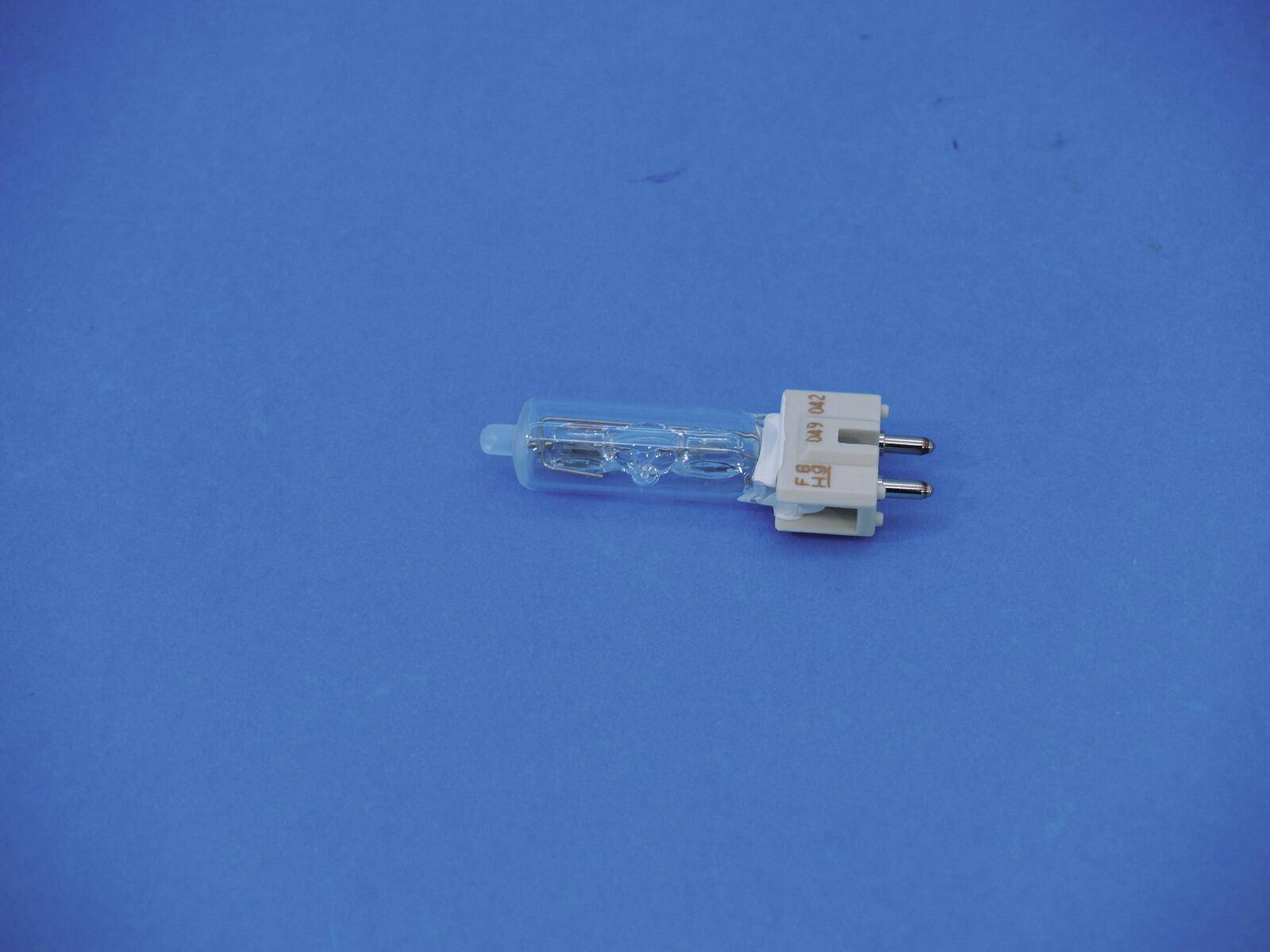 Eine kleine, klare Halogenglühlampe mit zwei Metallstiften liegt auf einer blauen Oberfläche.