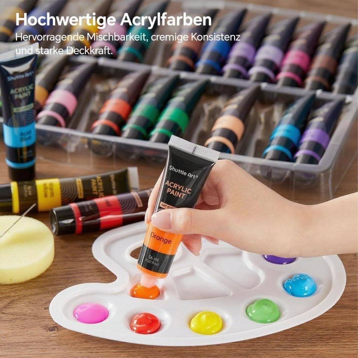 Eine Person drückt orangefarbene Acrylfarbe aus einer Tube auf eine Palette. Im Hintergrund sind verschiedene farbige Farbtuben auf einem Tisch zu sehen.