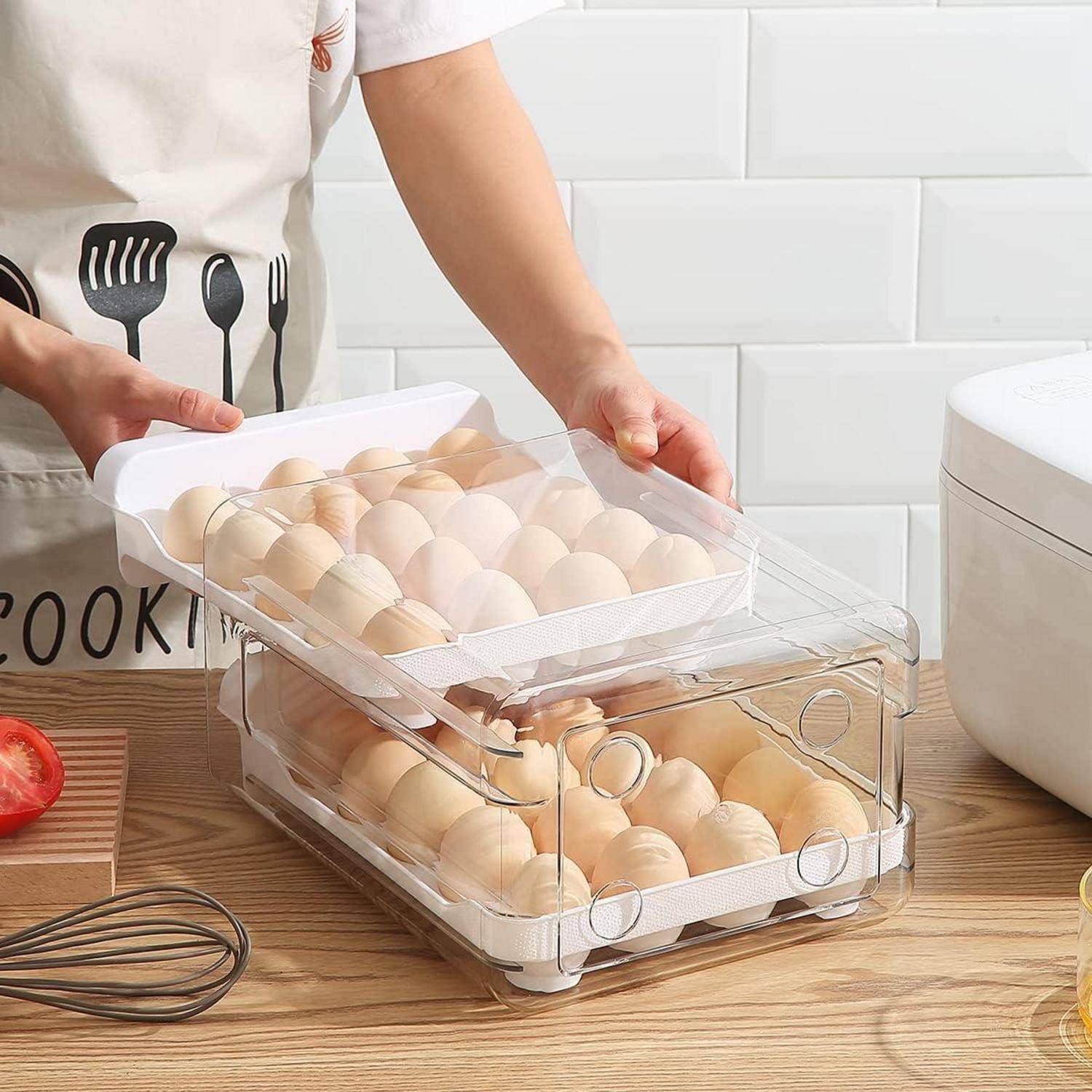 Eine Person ordnet Eier in einem transparenten Aufbewahrungsbehälter auf der Küchenarbeitsplatte an, neben einer Tomate, einem Schneebesen und einem Reiskocher.