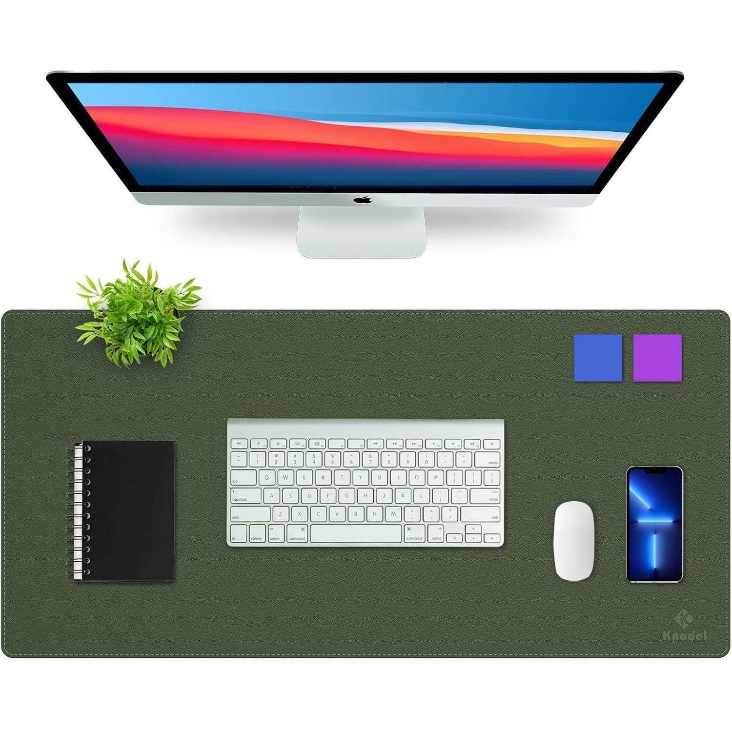Eine minimalistische Schreibtischeinrichtung zeigt einen Computermonitor, eine Tastatur, ein Smartphone mit blauem Bildschirm, einen Notizblock, eine Topfpflanze und Schreibwaren.