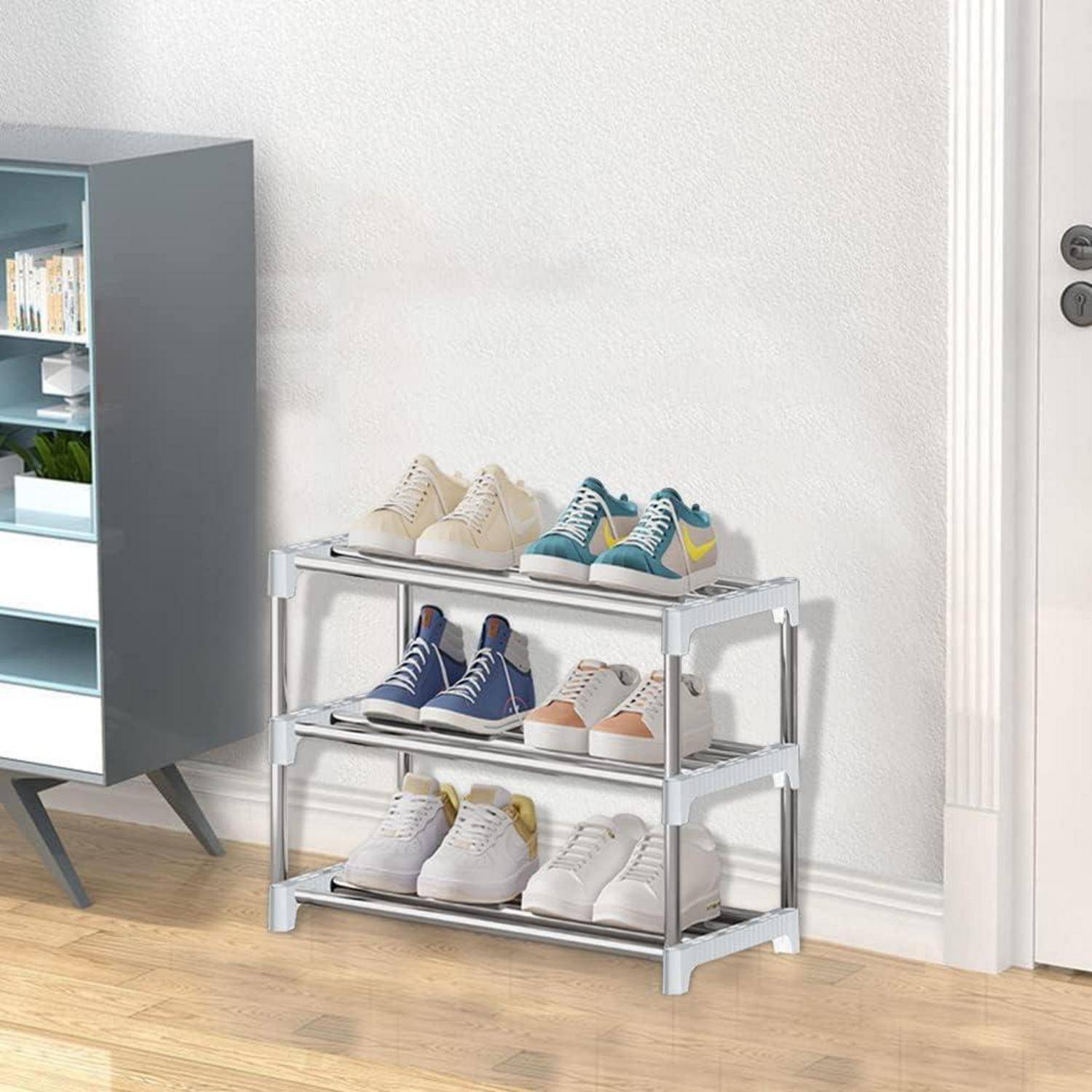 Ein weißes Schuhregal an einer hellen Wand hält sechs Paare ordentlich angeordneter Sneaker. Ein Schrank mit Pflanzen steht neben dem Regal.
