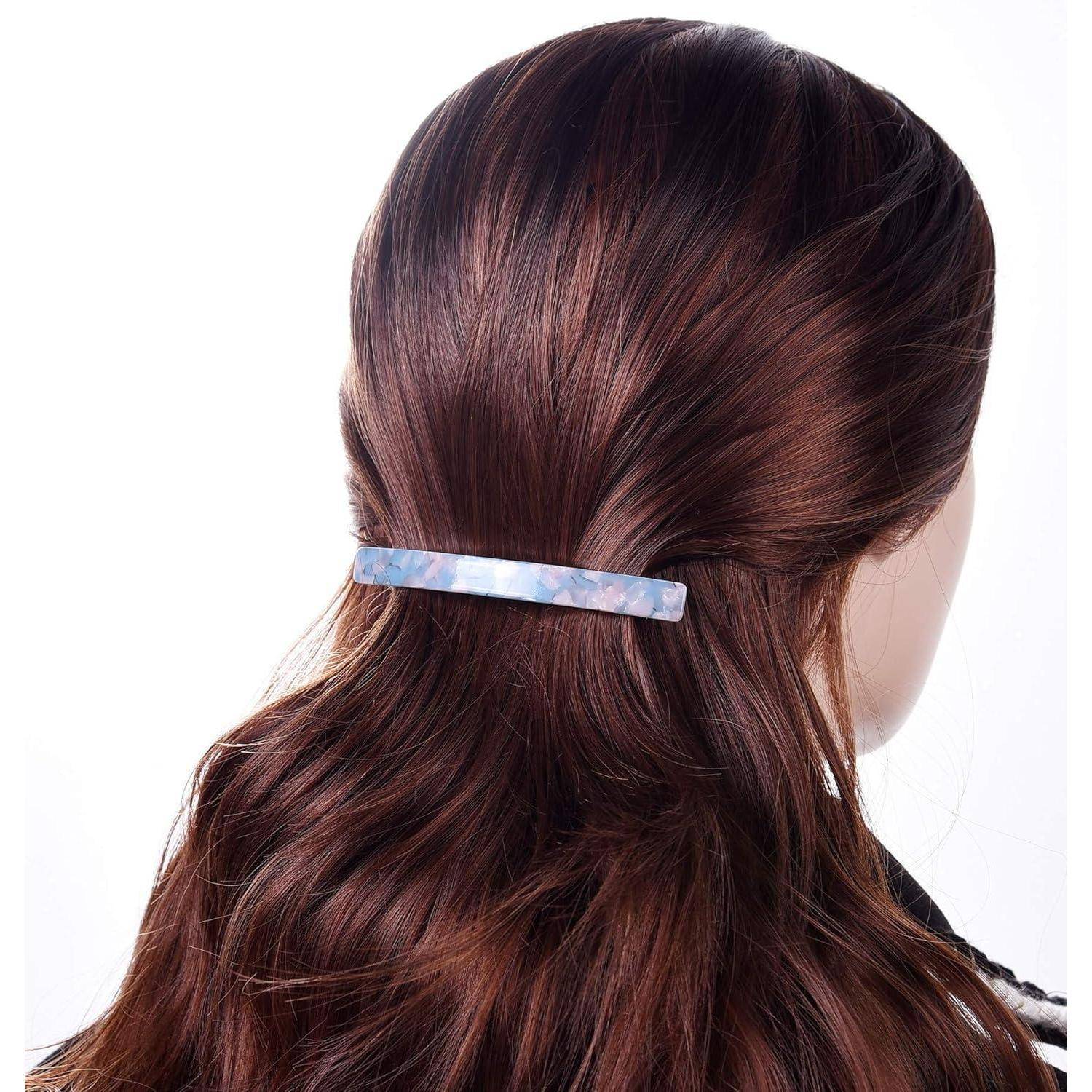 Eine Person mit langen braunen Haaren, die mit einer blauen Haarspange befestigt sind, wird von hinten gezeigt, wobei das Haaraccessoire und die Frisur hervorgehoben werden.