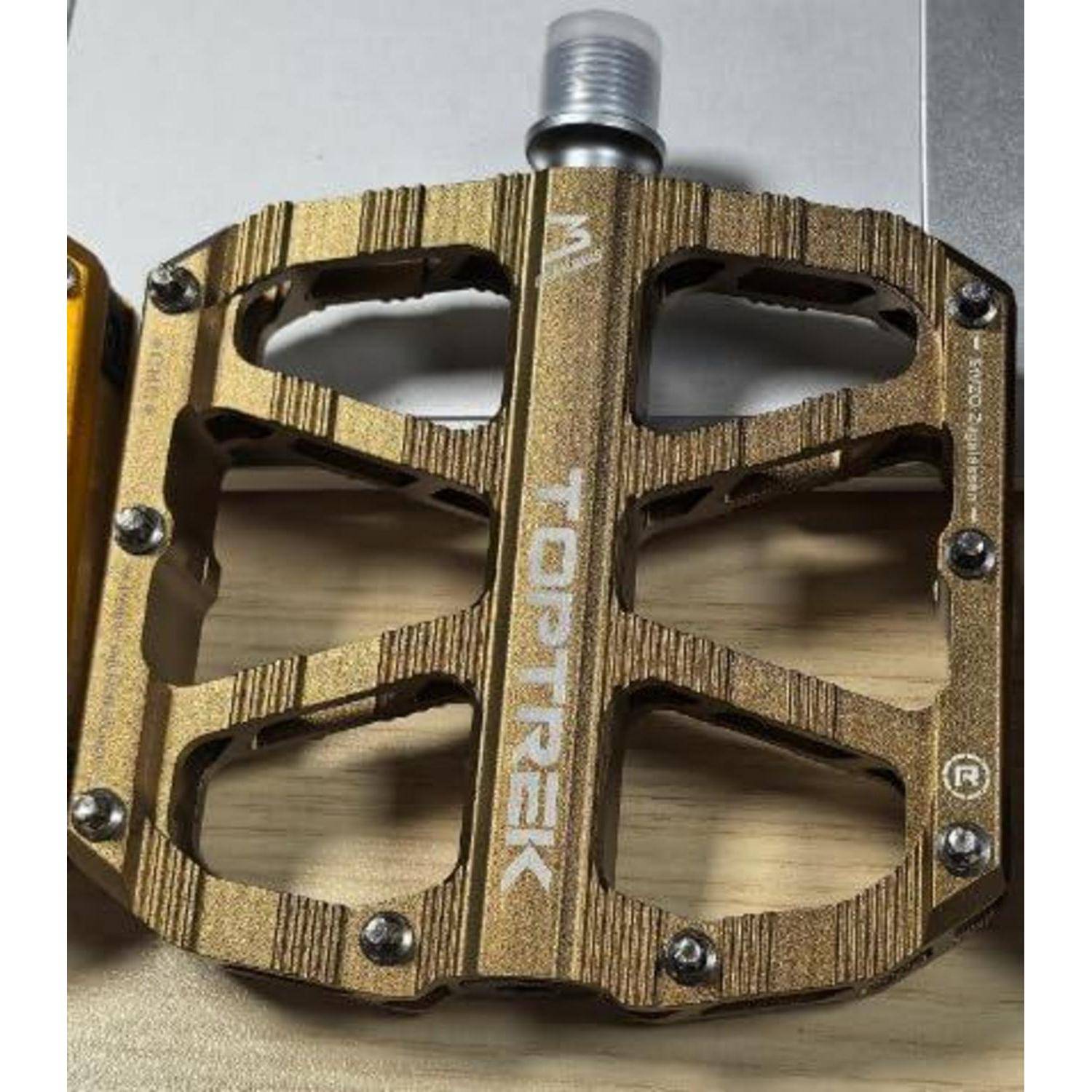 Ein Metall-Fahrradpedal mit strukturierter, goldener Oberfläche. Die Marke 'Toptrek' ist auf der Oberfläche des Pedals gedruckt.