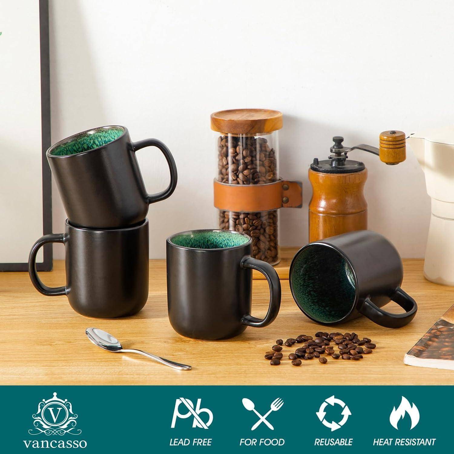Drei schwarze Tassen mit grünem Inneren, aufeinander gestapelt und auf einem Tisch neben einer Kaffeemühle angeordnet, mit verstreuten Kaffeebohnen.