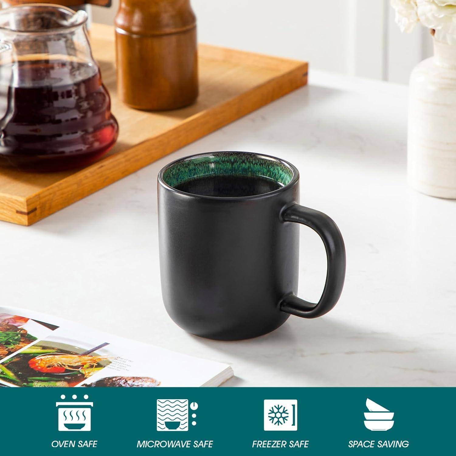 Eine schwarze Tasse auf einer Küchenarbeitsplatte mit Kaffee, daneben ein Holztablett mit einer Karaffe. Text am unteren Rand hebt Merkmale hervor: backofenfest, mikrowellengeeignet, gefrierschrankfest und platzsparend.