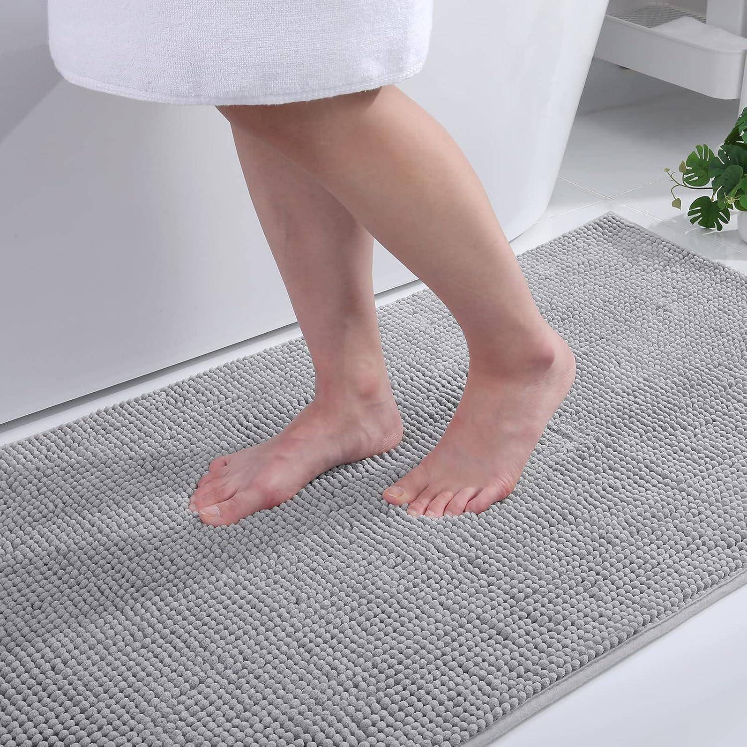 Nackte Füße, die auf einem strukturierten grauen Badvorleger neben einer weißen Badewanne auftreten und Komfort und Sauberkeit in einer Badezimmeratmosphäre vermitteln.