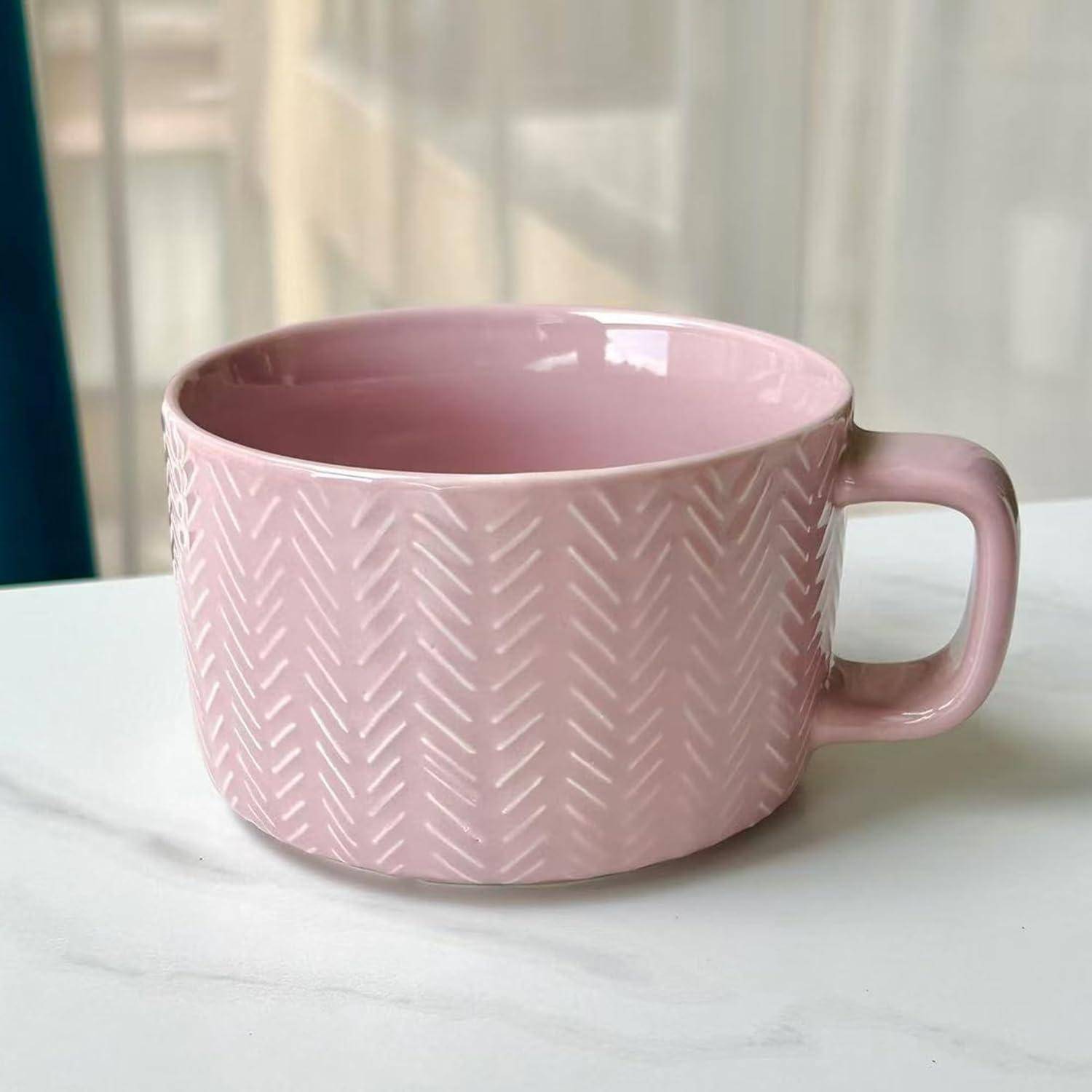 Eine pinke Keramiktasse mit einem strukturierten Zickzackmuster steht auf einer weißen Oberfläche, während Licht durch ein Fenster im Hintergrund fällt.