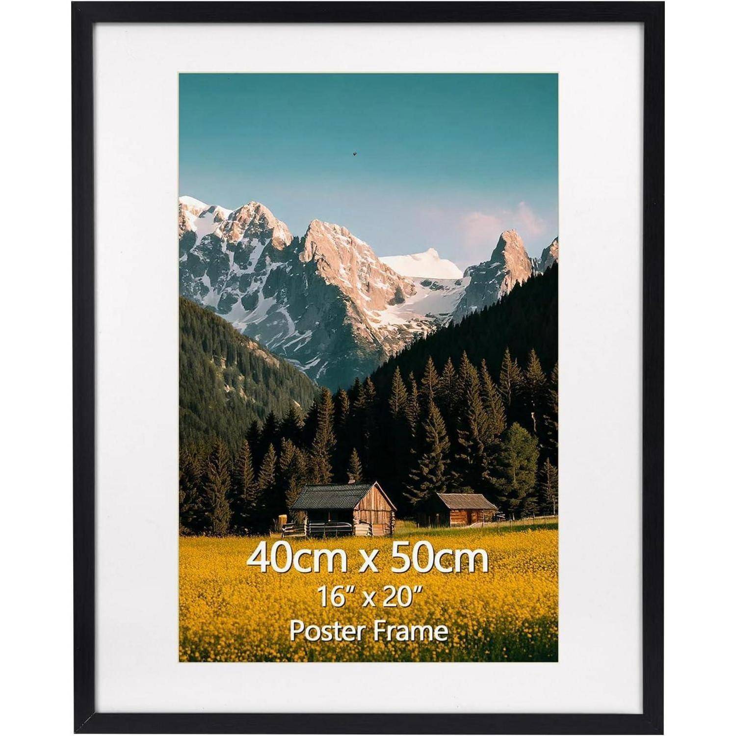 Ein Posterrahmen, der eine Fotografie einer Berglandschaft mit schneebedeckten Gipfeln, Wald und kleinen Holzhütten in einer Wiese zeigt.