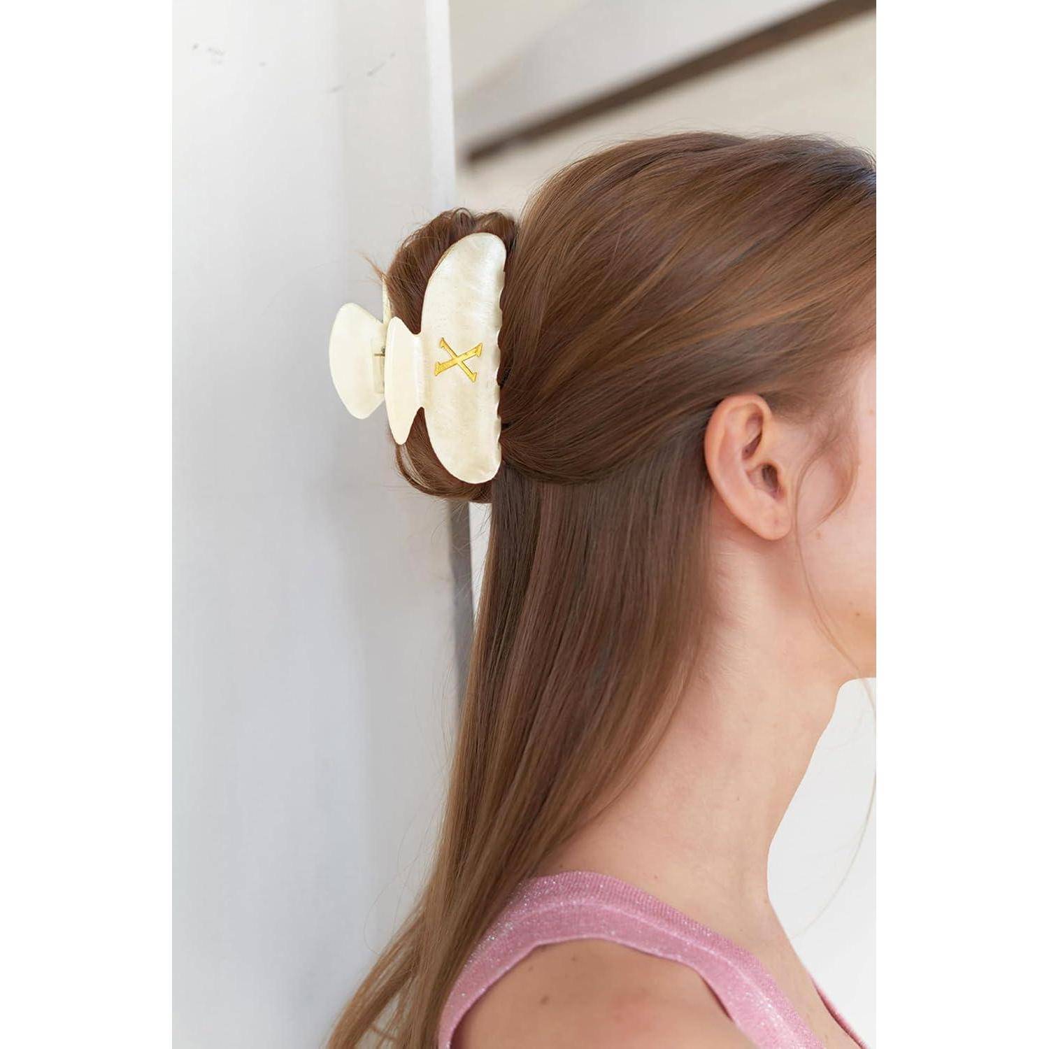 Eine Frau mit langen braunen Haaren trägt eine große, cremefarbene Haarspange in Form eines Schmetterlings. Sie trägt ein rosa Oberteil.