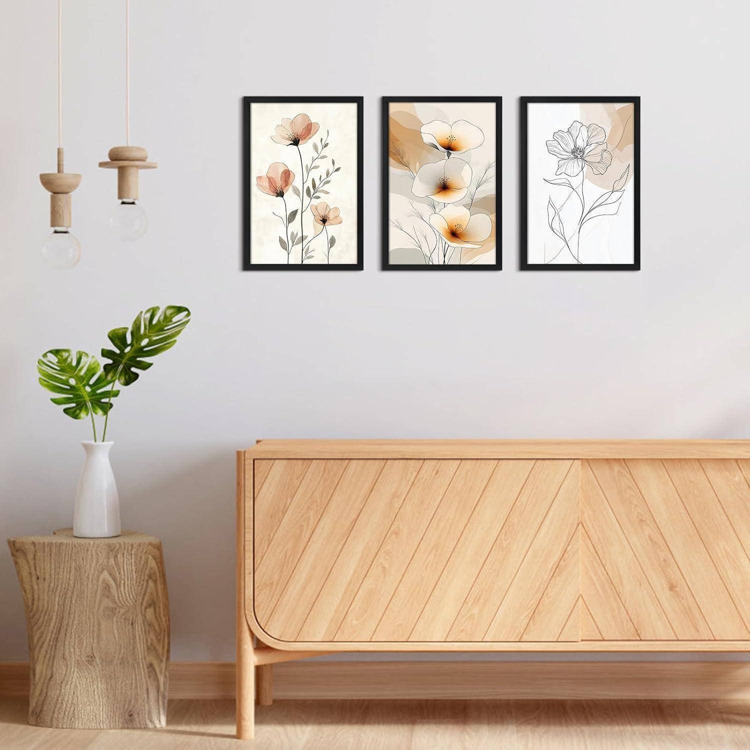 Drei gerahmte Blumenkunstwerke in neutralen Tönen an einer hellen Wand über einer Holzbank mit einer Vase und Pendelleuchten, die eine ruhige Dekoration schaffen.