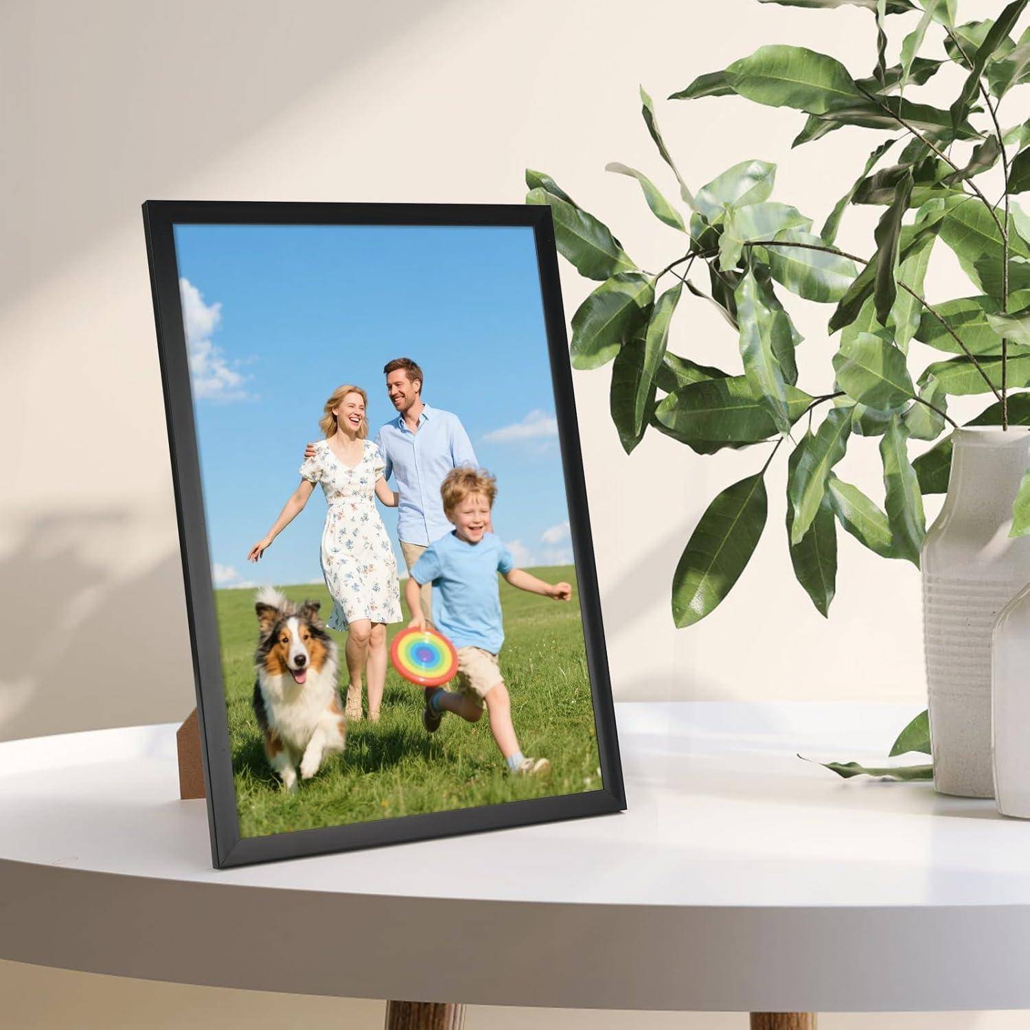 Ein gerahmtes Foto einer lächelnden Familie mit einem Hund und einer Frisbee-Scheibe, platziert auf einem runden weißen Tisch neben einer Zimmerpflanze mit Blättern.