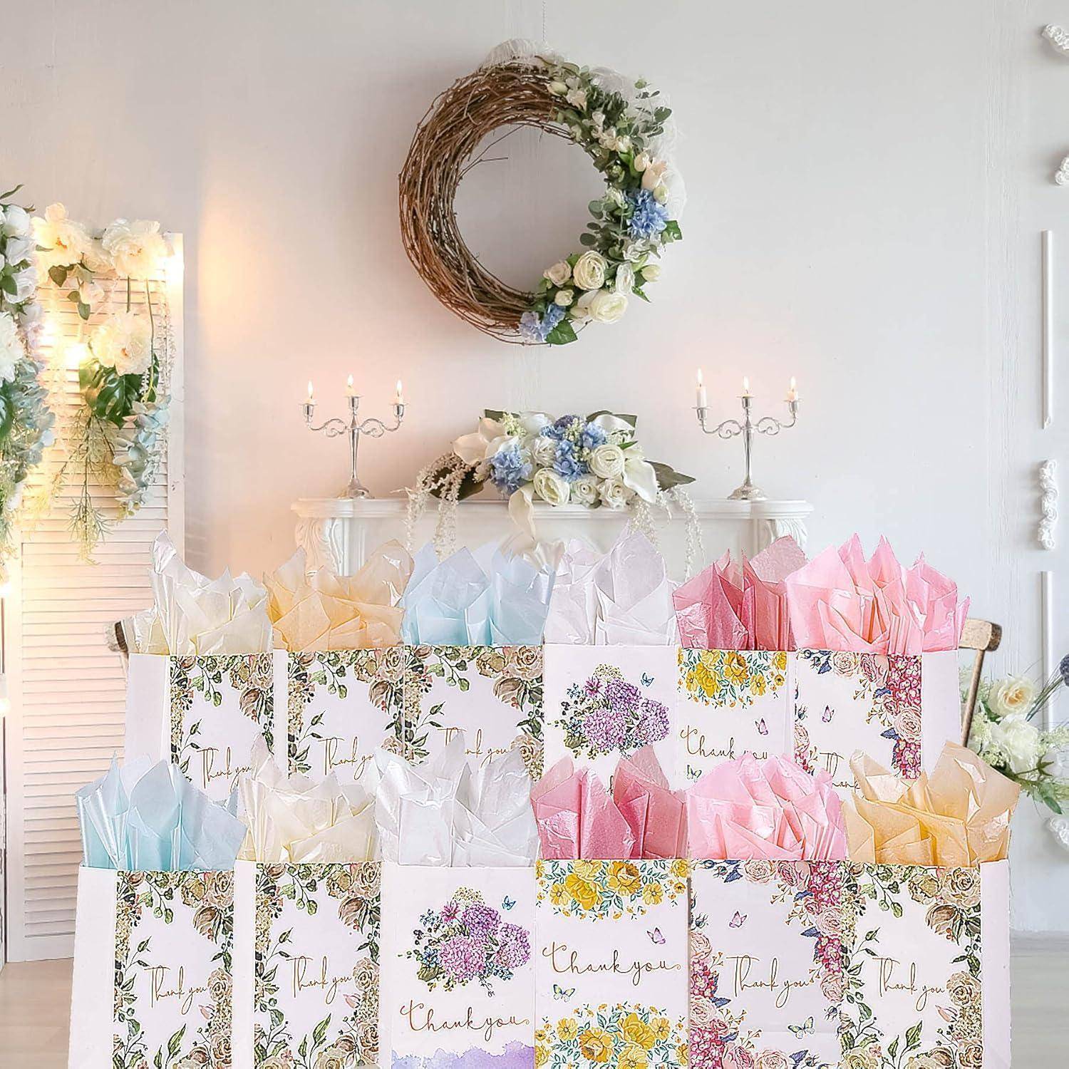 Geschenktüten mit Blumenmustern und 'Danke'-Aufschrift sind vor einer dekorierten Wand mit Kerzen und einem Kranz angeordnet.