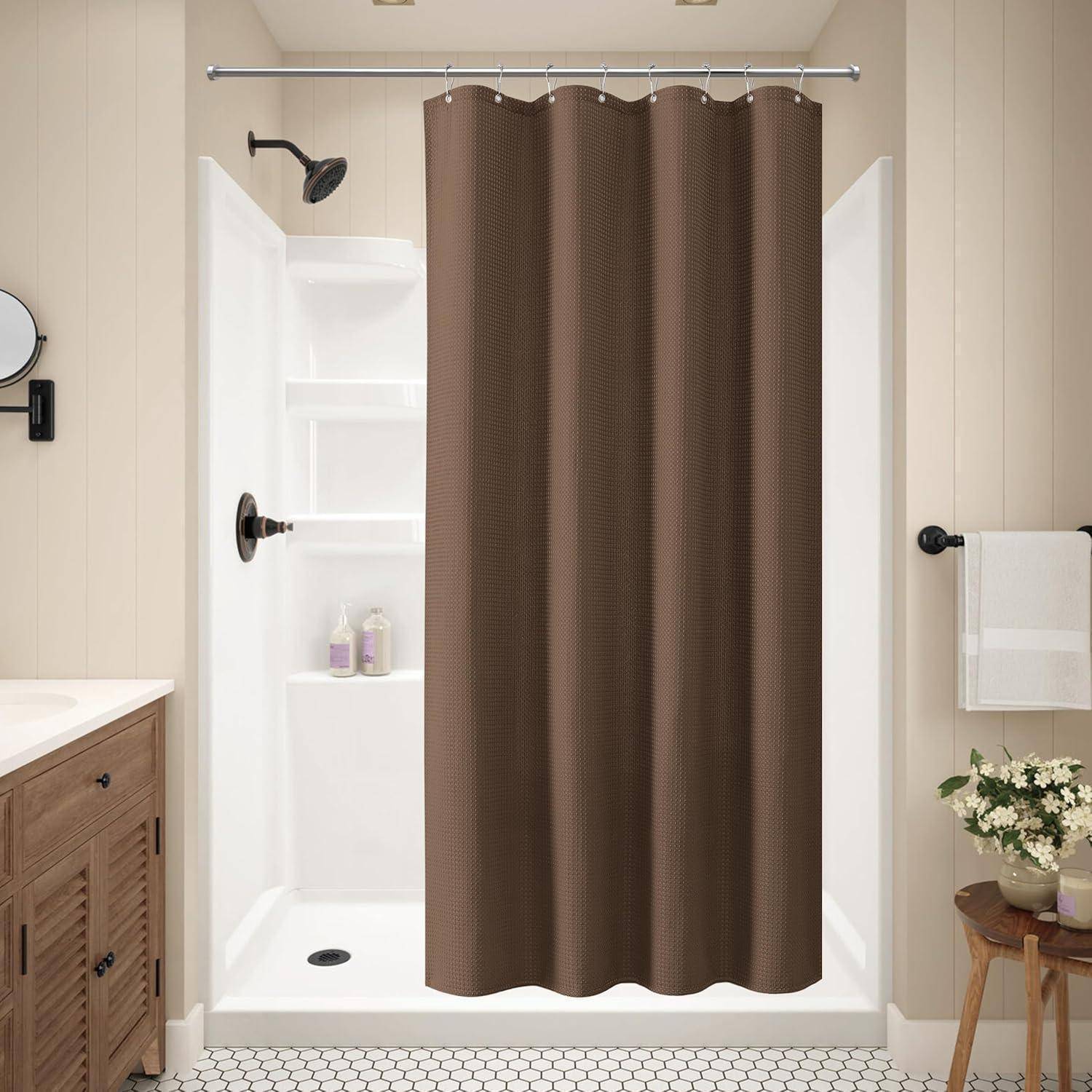 Badezimmer mit einem braunen Duschvorhang, weißer Duschkabine, Waschtisch, Spiegel, Handtuchhalter mit einem Handtuch und einer Blumenvase.