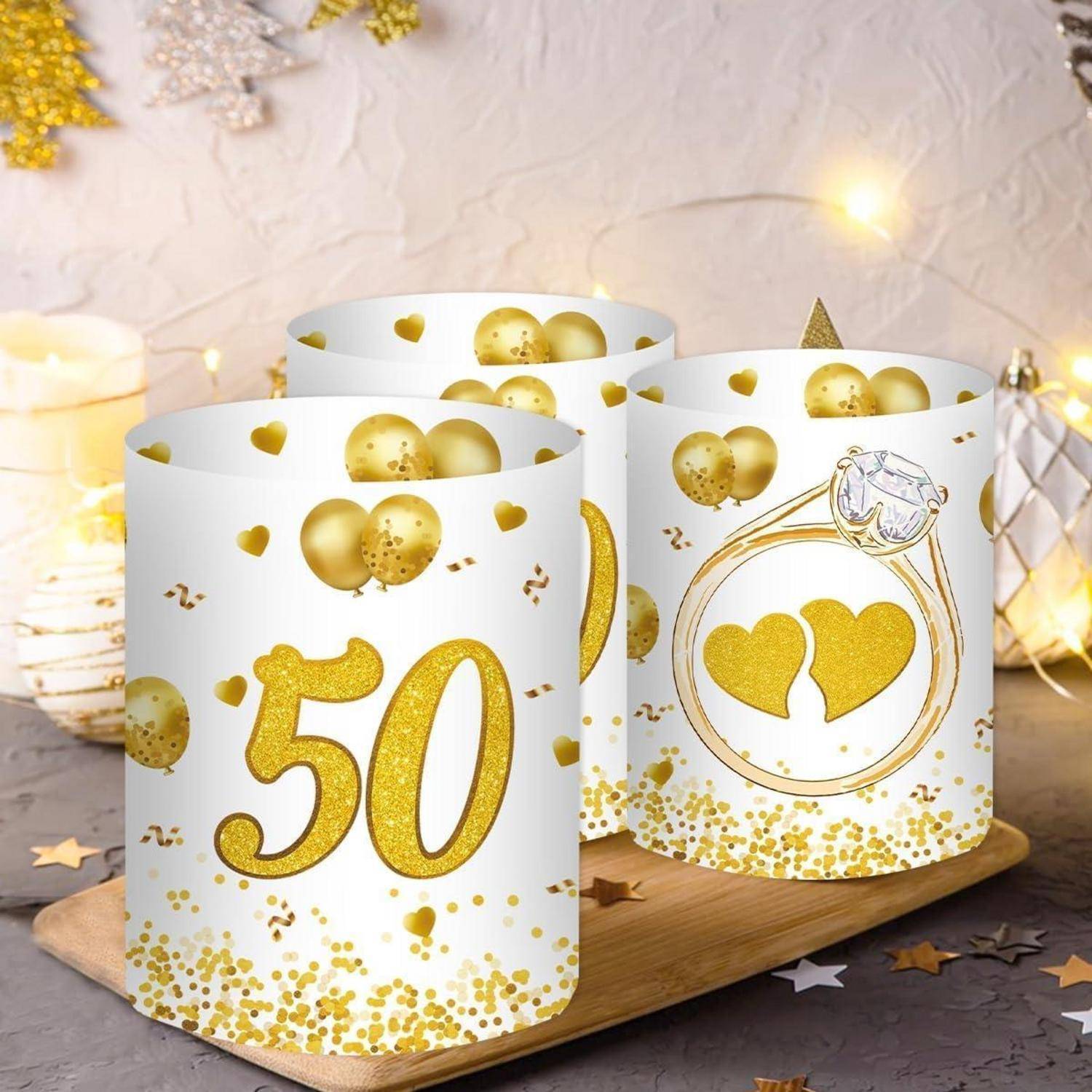 Drei dekorative Kerzen mit goldenen Details. Eine Kerze zeigt eine große '50', eine andere einen Ring mit zwei Herzen und die dritte Kerze trägt Luftballons.
