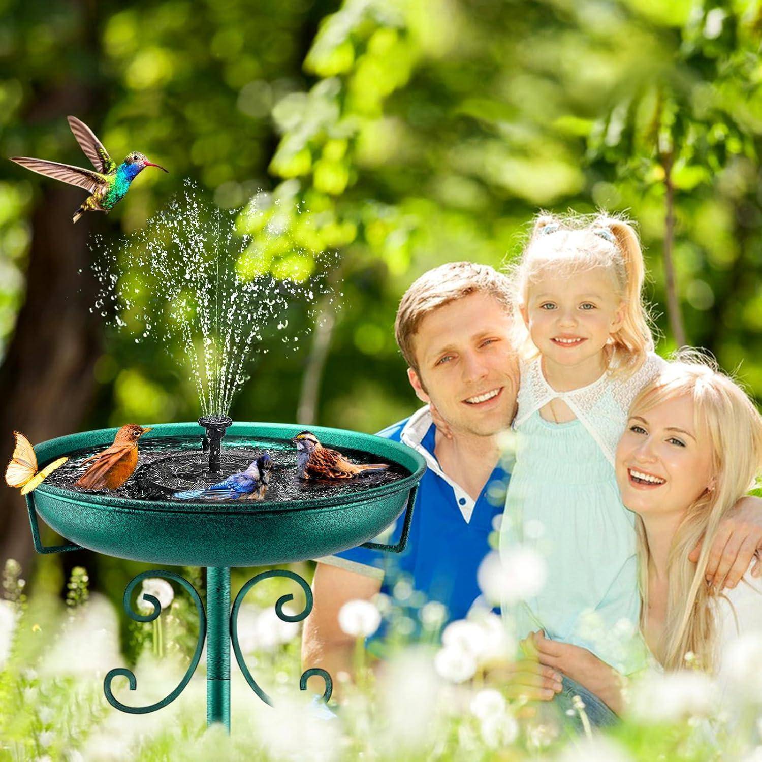 Eine Familie mit drei Personen lächelt in einem Garten neben einem Vogeltränkstein mit bunten Vögeln und einem plätschernden Brunnen; ein Kolibri fliegt in der Nähe.