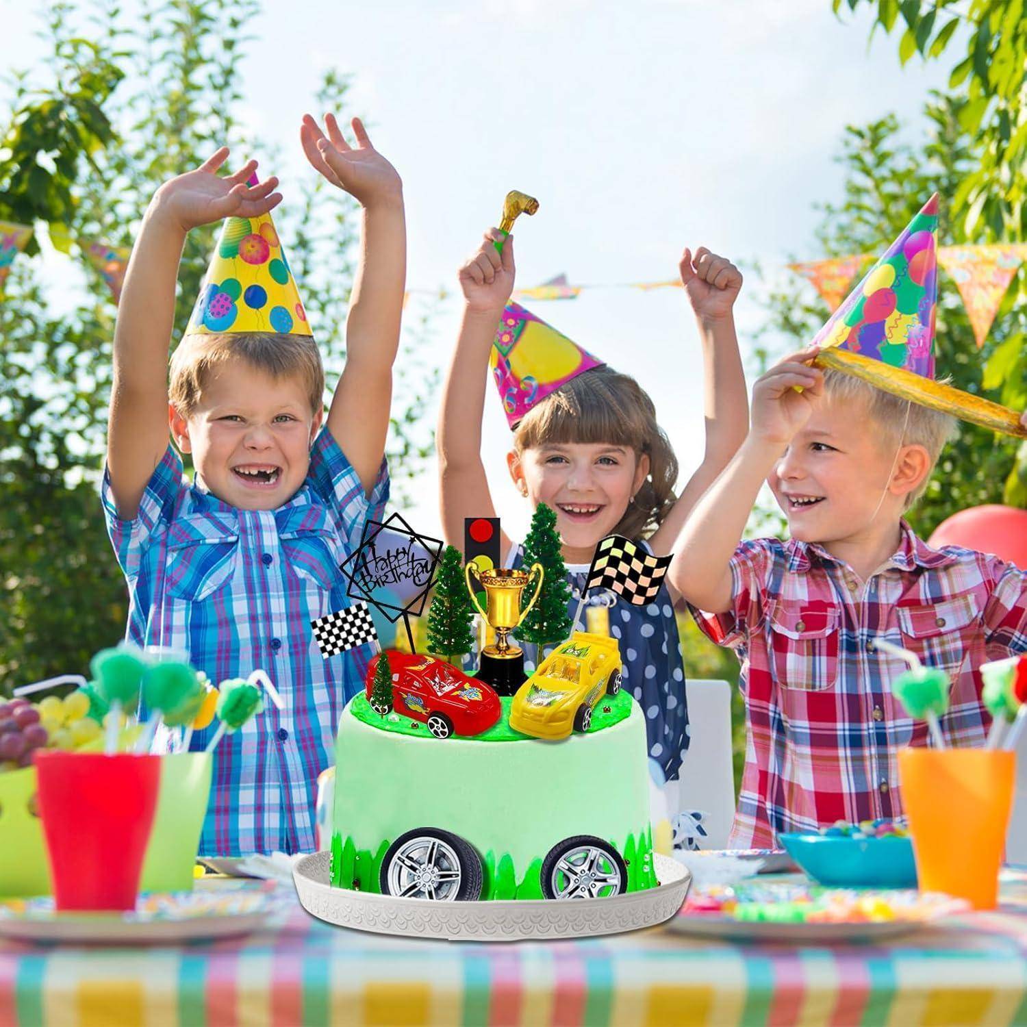 Kinder bei einer Geburtstagsparty feiern mit einer dekorierten Auto-Themen-Torte, tragen Partyhüte und lächeln an einem sonnigen Tag im Freien.
