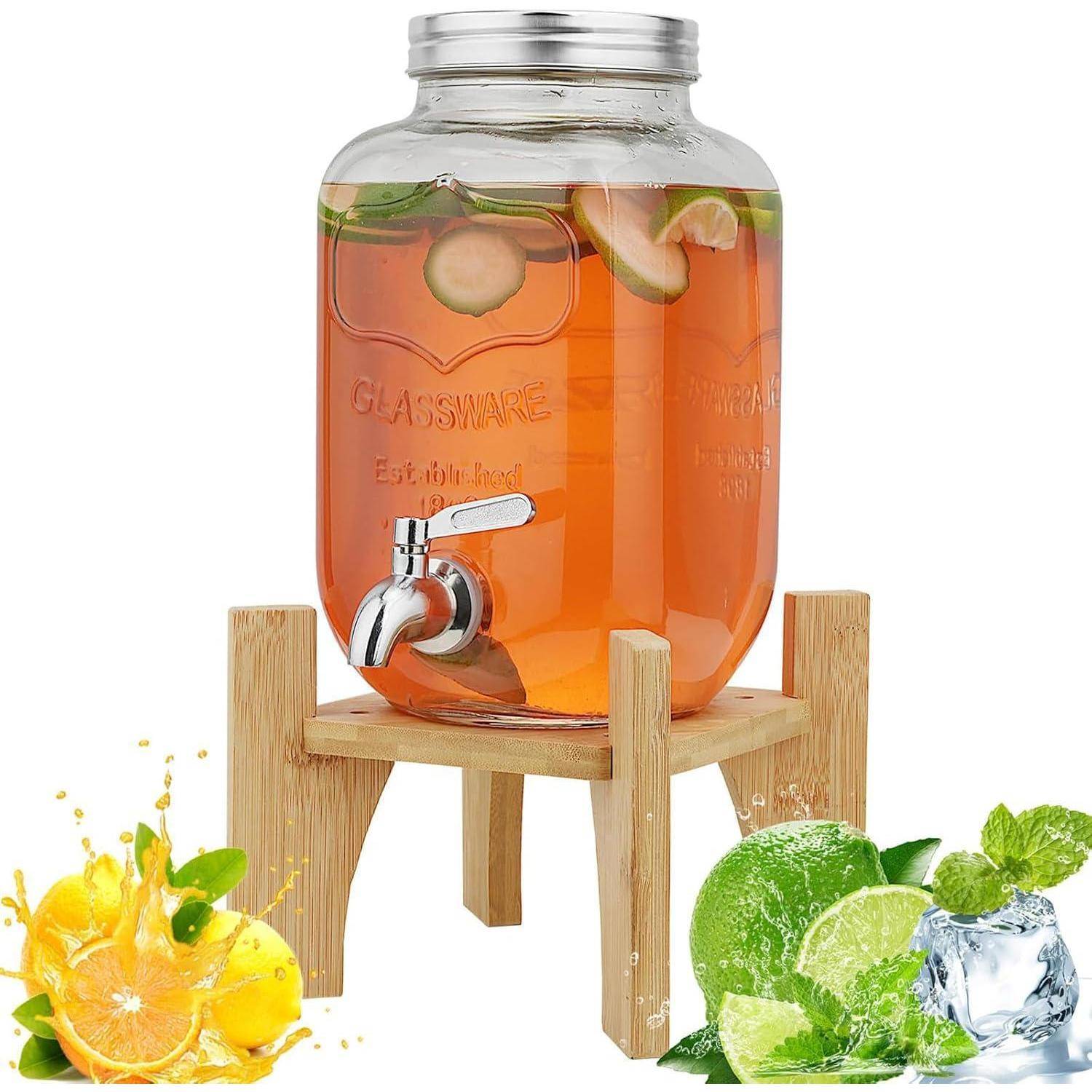 Ein Getränkespender aus Glas mit Zapfhahn, gefüllt mit fruchtinfundierter Flüssigkeit, auf einem Holzständer. Mit Zitrusscheiben dekoriert.
