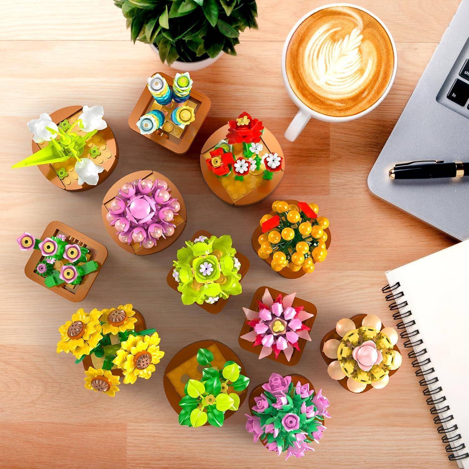 Eine Vielzahl bunter blumenförmiger Teile aus LEGO-Steinen ist auf einem Tisch neben einem Latte, einem Stift und einem Notizbuch angeordnet.